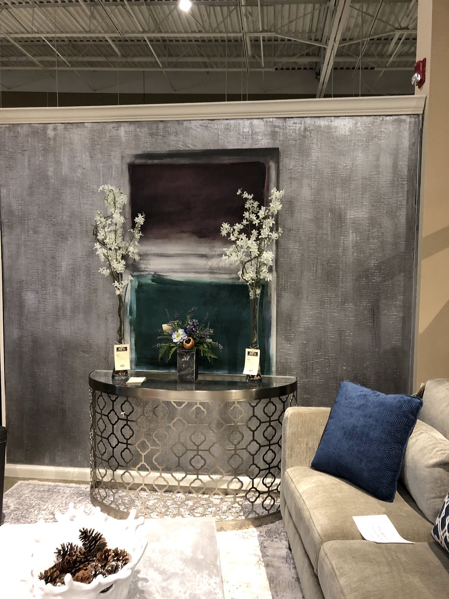 A decorative console with art, flowers, and a sofa against a gray textured wall.