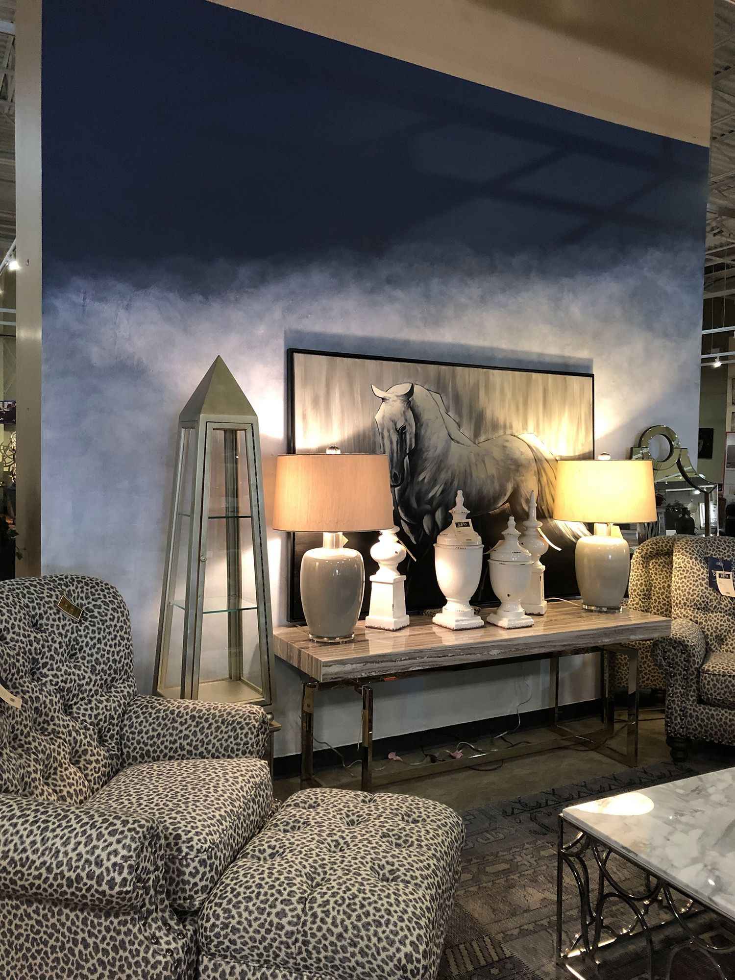 Living room furniture display: cheetah-print chair, console table with lamps, horse art on a blue and white painted wall.