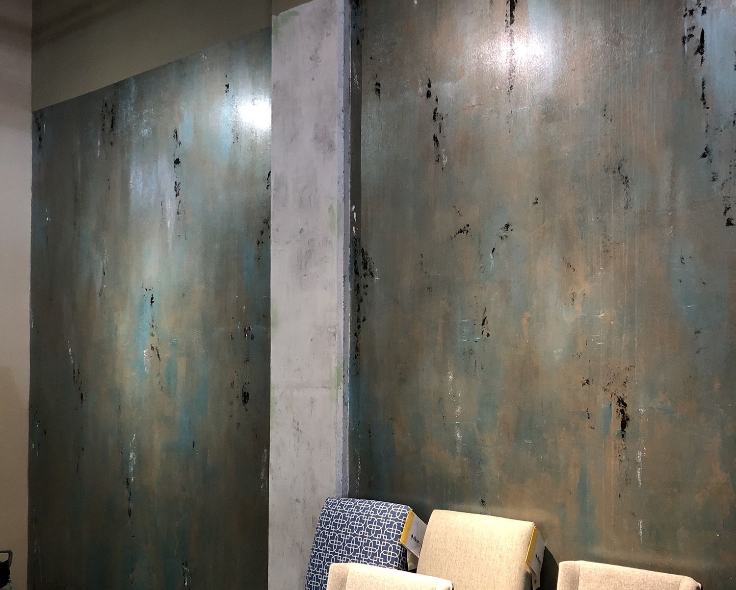 Textured teal wall with a concrete pillar, displaying decorative fabrics.