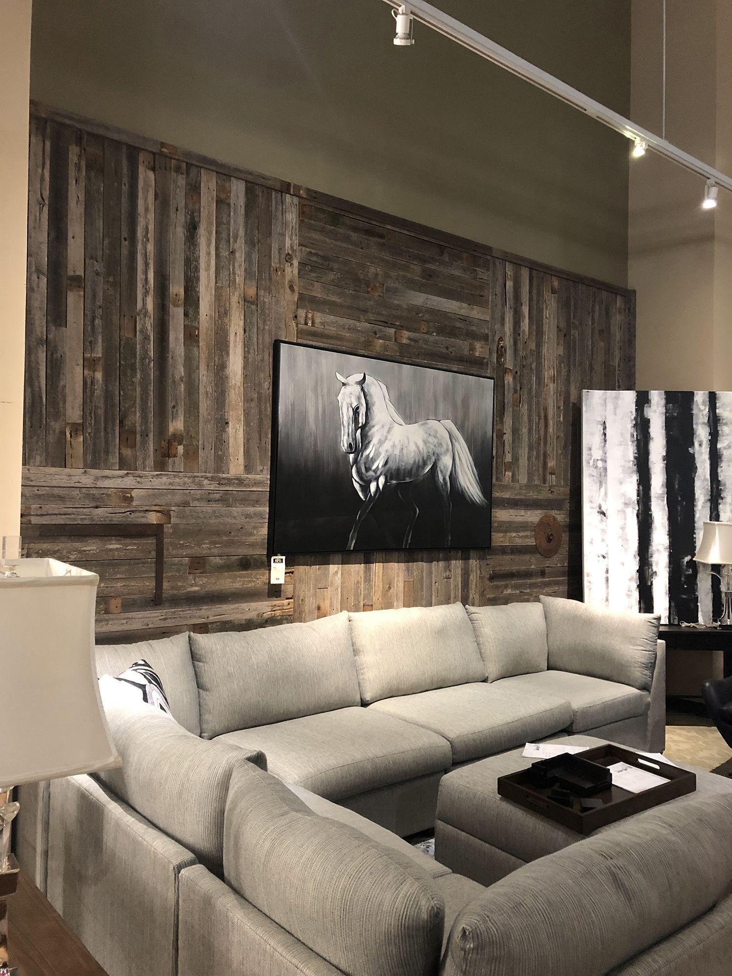 Living room with sectional sofa, wood paneled wall, and artwork of a horse and abstract black and white painting.