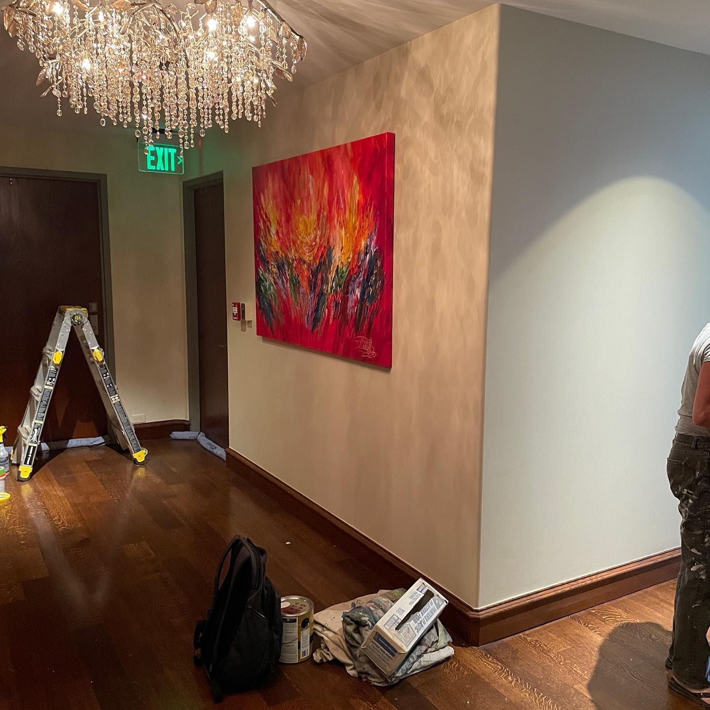 Hallway with artwork, chandelier, and a person painting the wall.