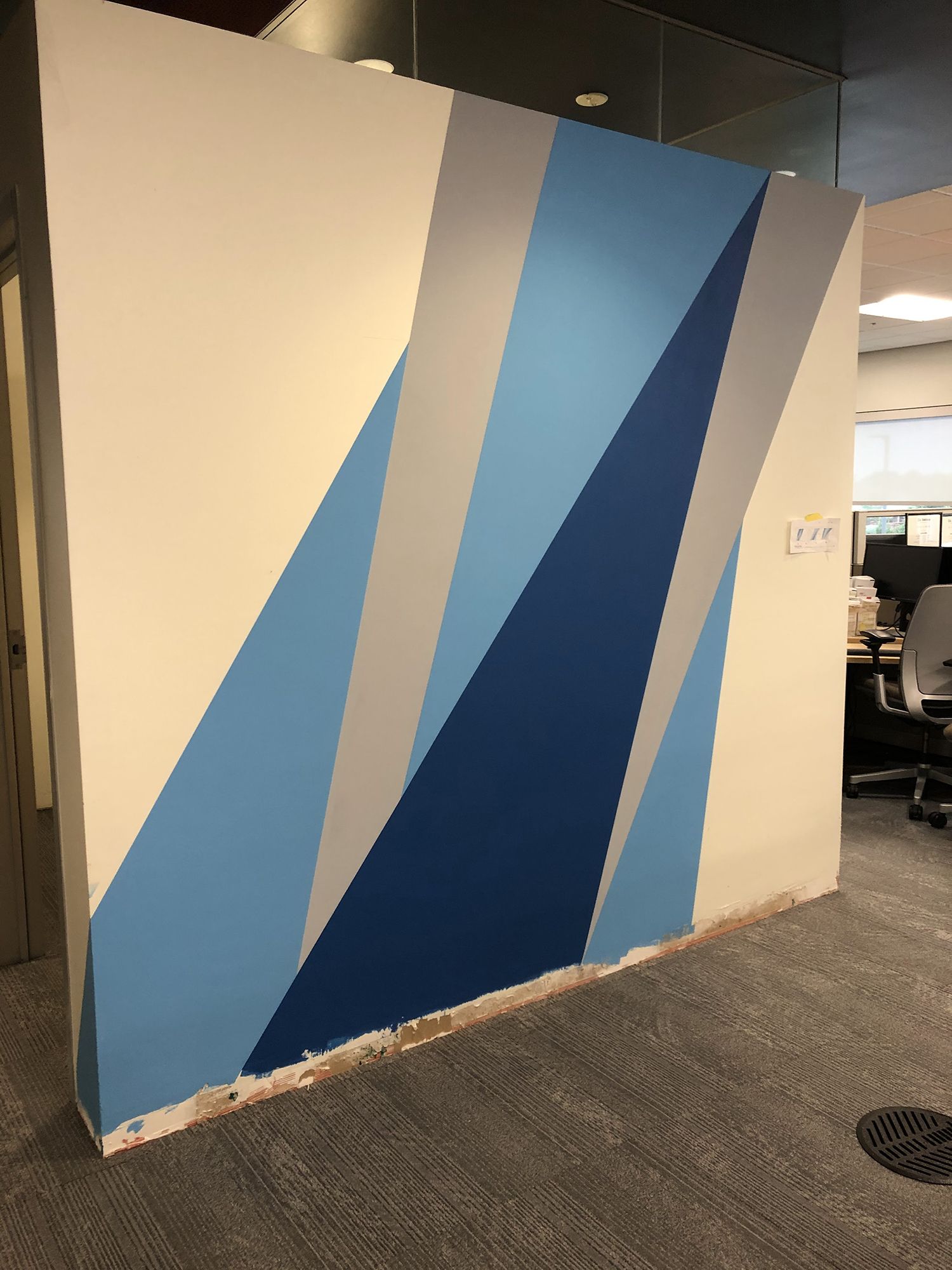 Wall painted with abstract geometric design in blue, gray, and white, in an office setting.