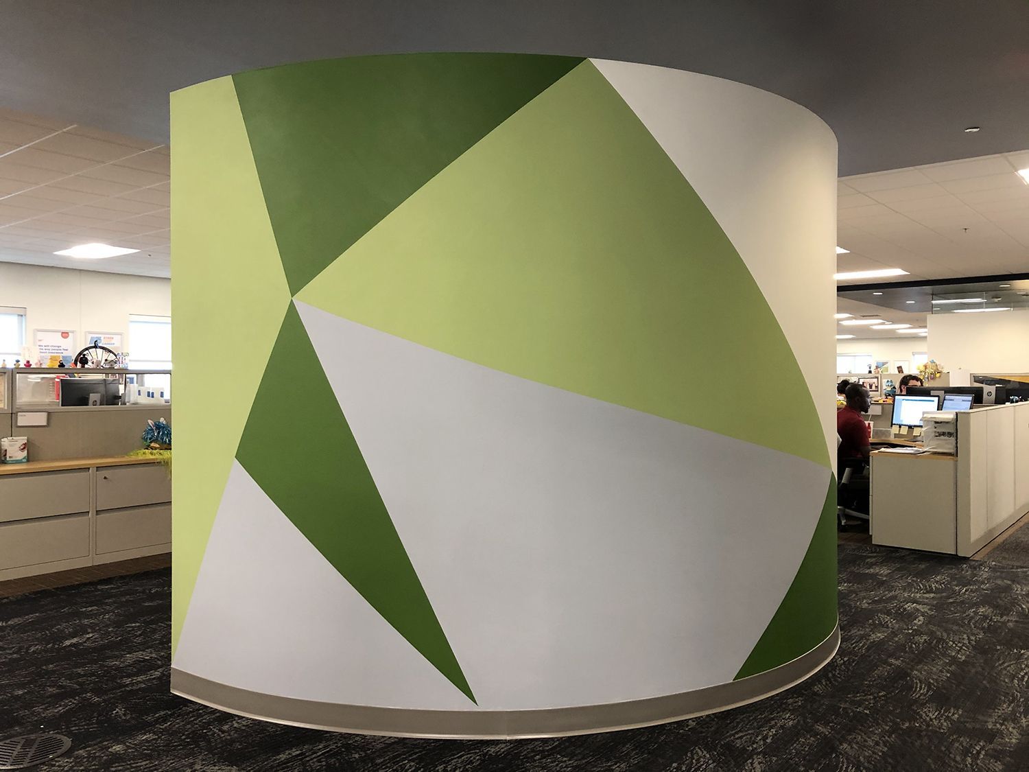 Cylindrical column in office space with geometric design in green and white colors.