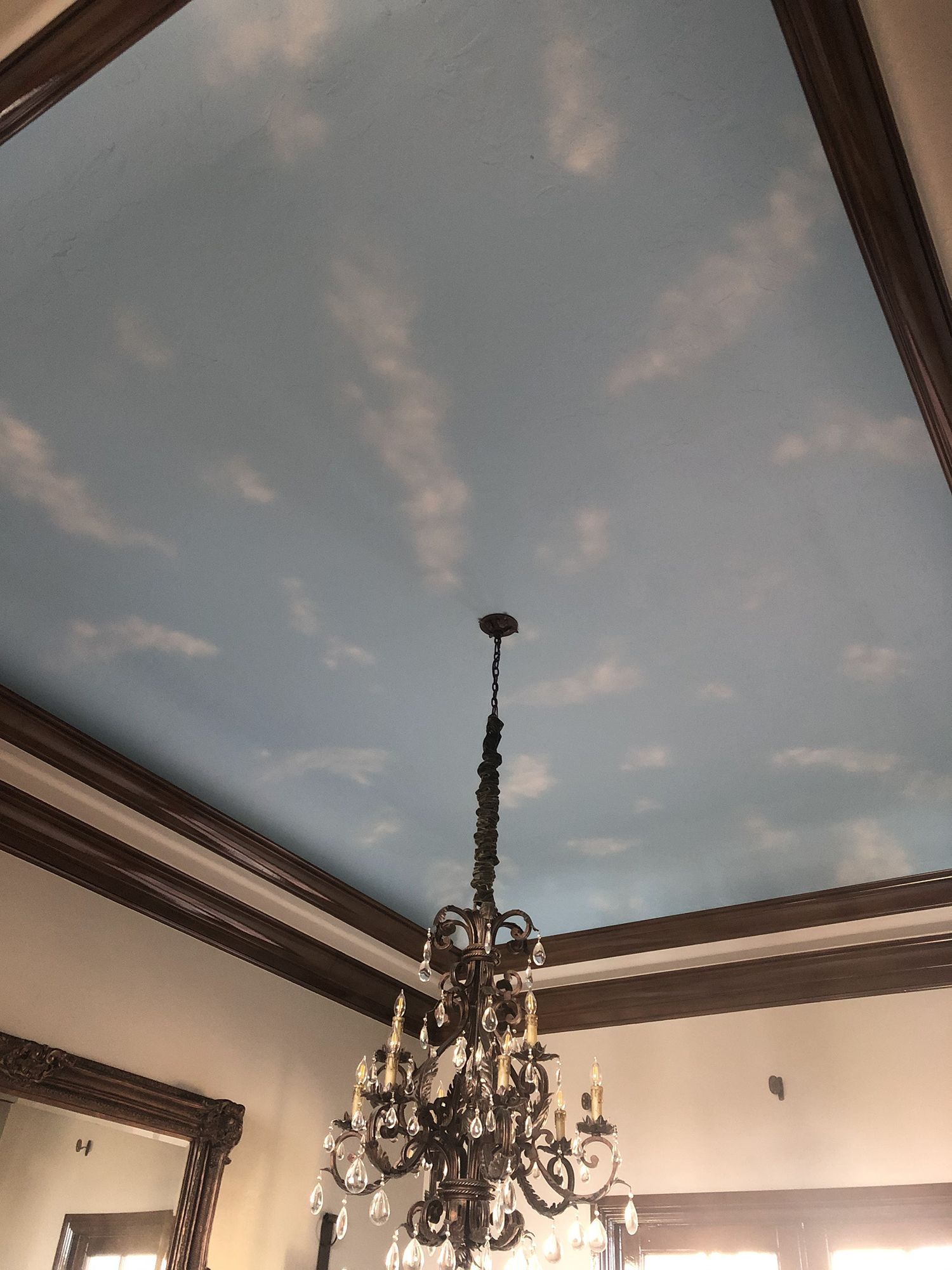 Sky-painted ceiling with white clouds, dark chandelier hanging below, framed by dark wood trim.