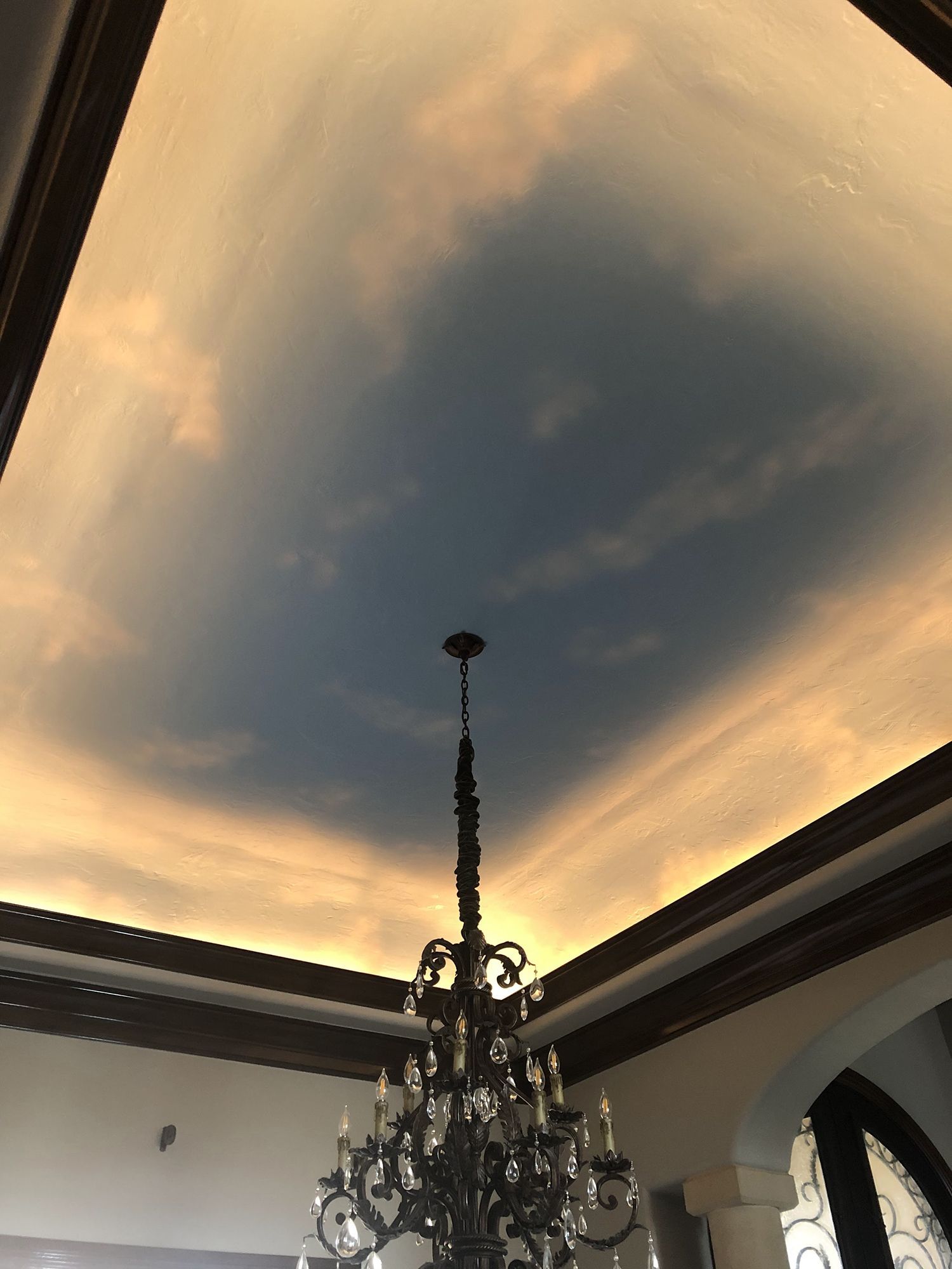 Ceiling painted as a sky with clouds, a chandelier hangs below.
