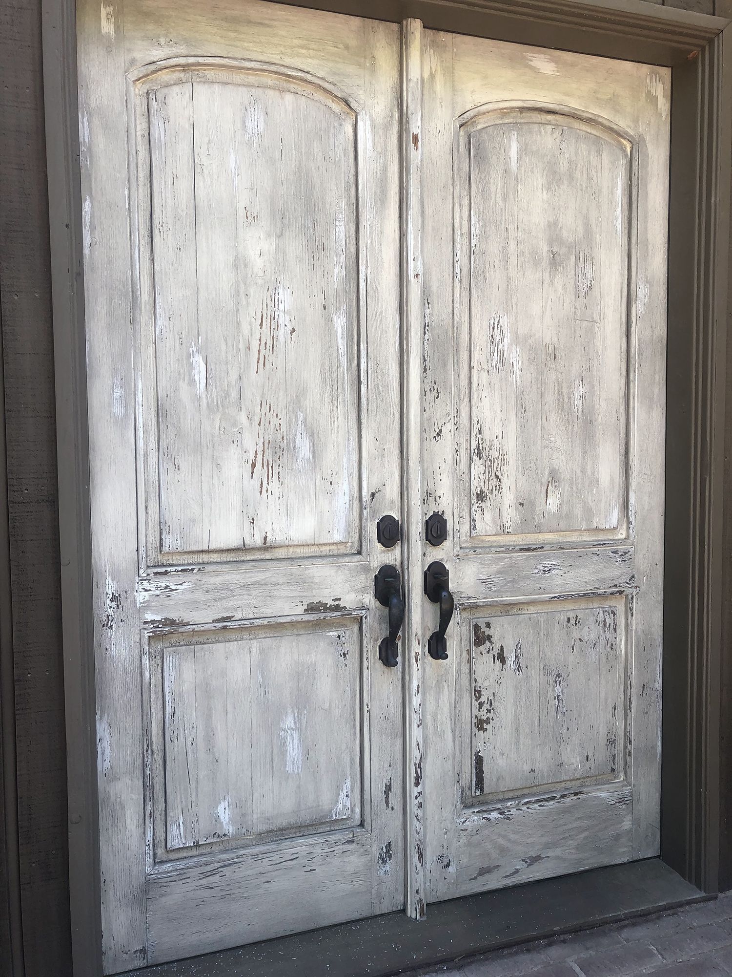 White, distressed double doors with black handles, set in a brown door frame.