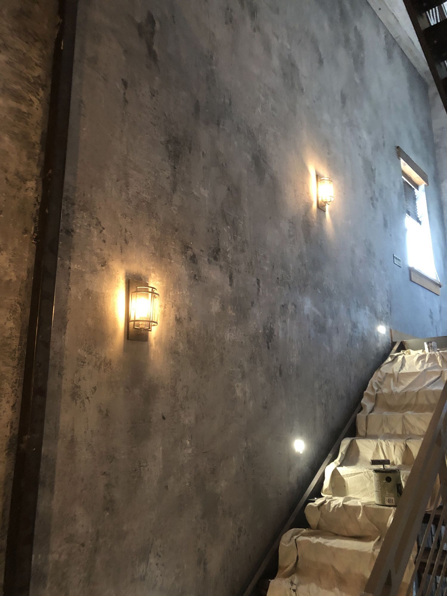 Gray textured wall with two sconce lights and a staircase.