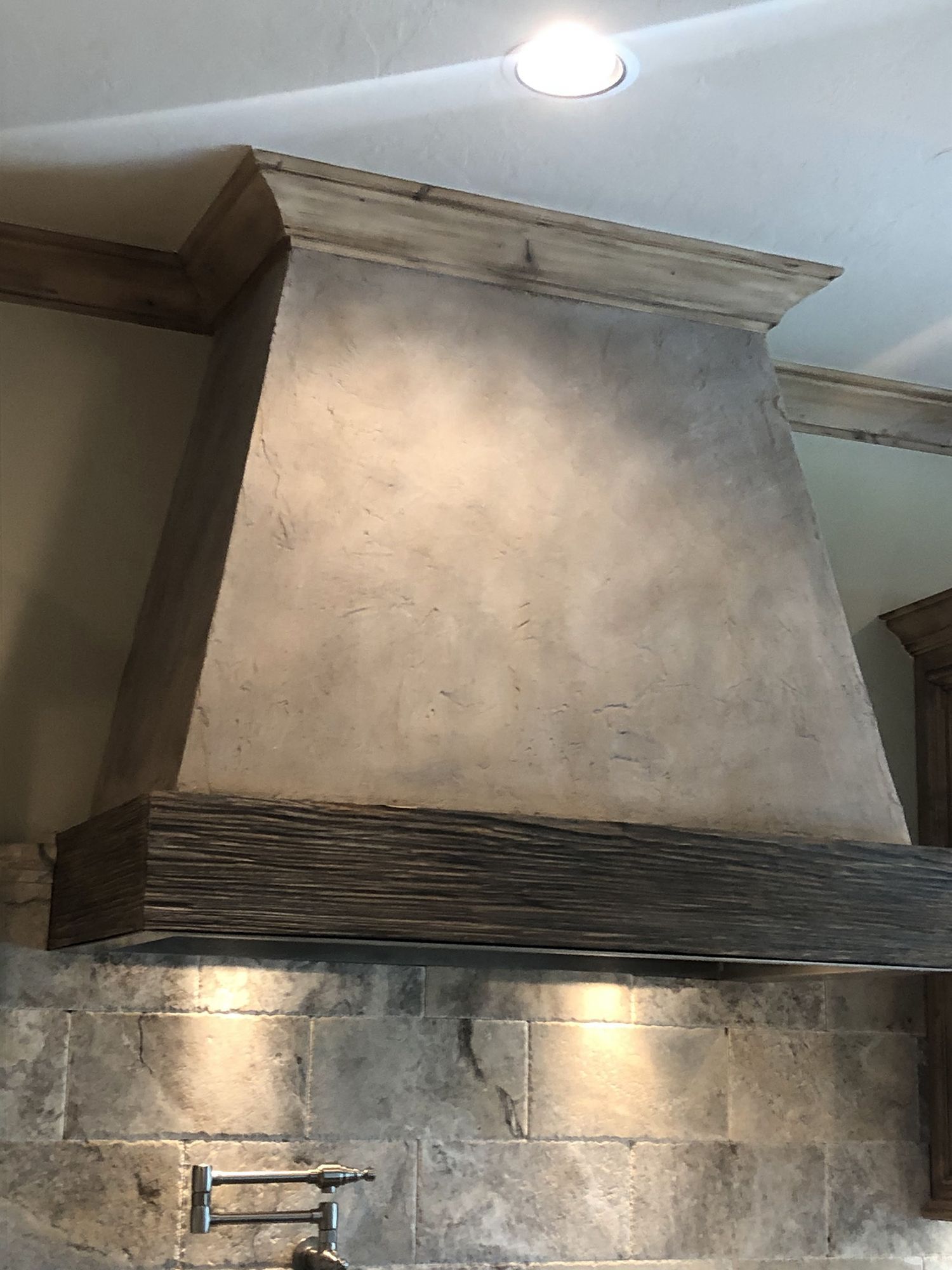 Gray concrete kitchen range hood with wood trim and stone backsplash.