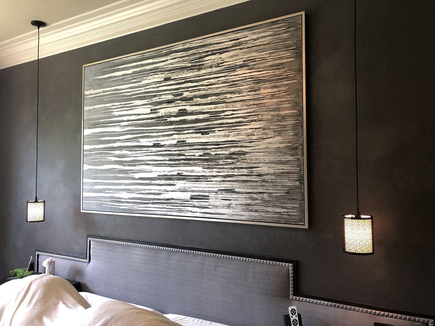Bedroom with large abstract art, pendant lights, gray headboard, and dark gray wall.