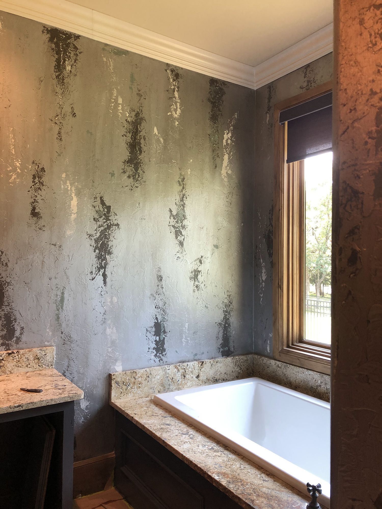 Bathroom with patterned gray and white wallpaper, bathtub, and window with a view.