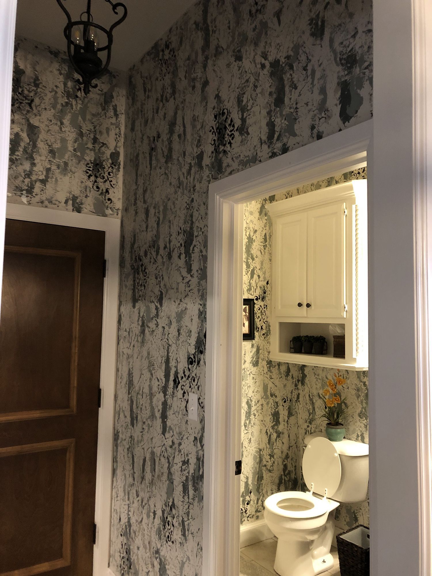 Hallway with abstract gray and white wallpaper, leading to a bathroom with a toilet and cabinet.