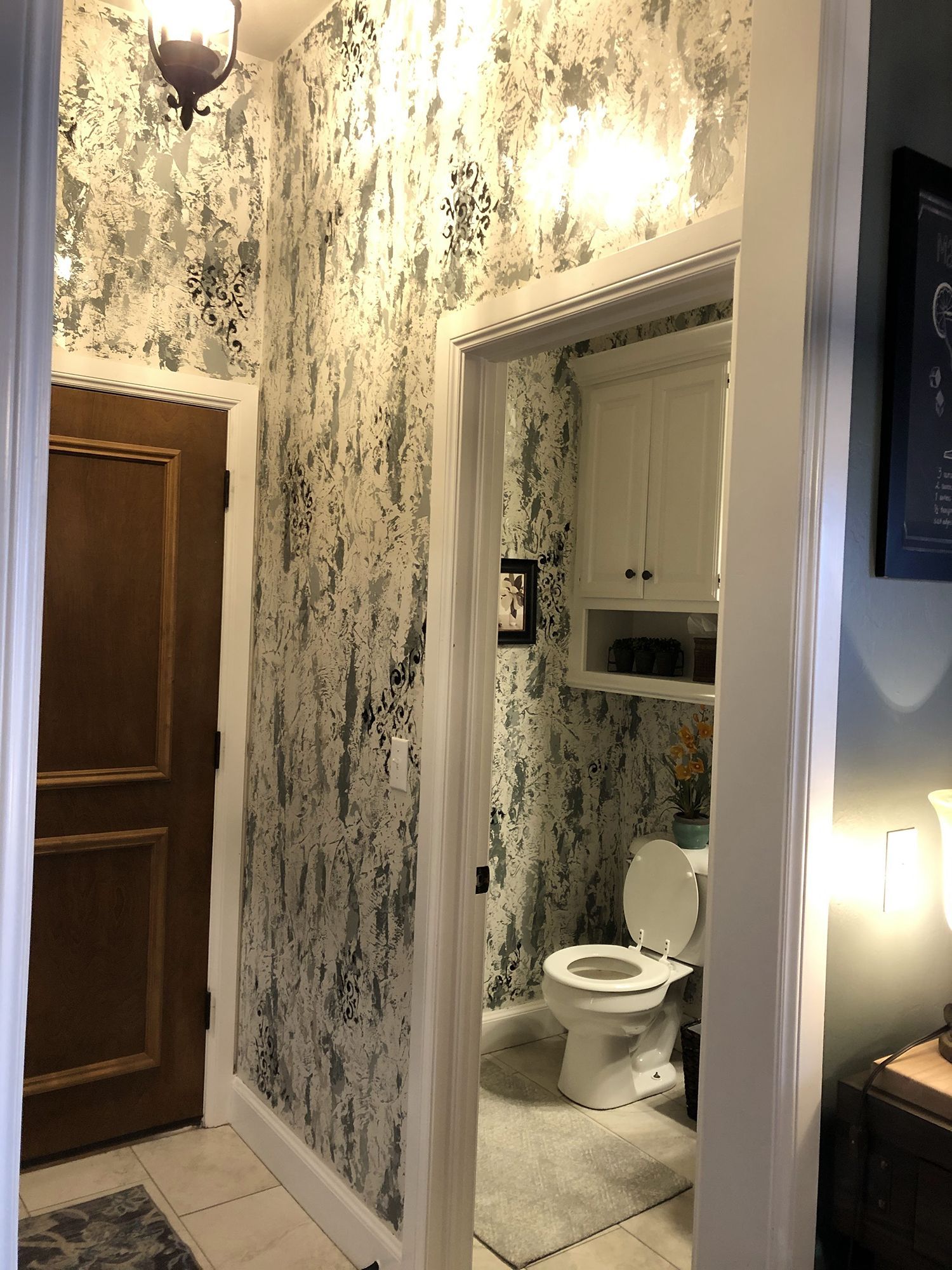 Hallway with decorative wallpaper, leading to a bathroom with a toilet and cabinet.