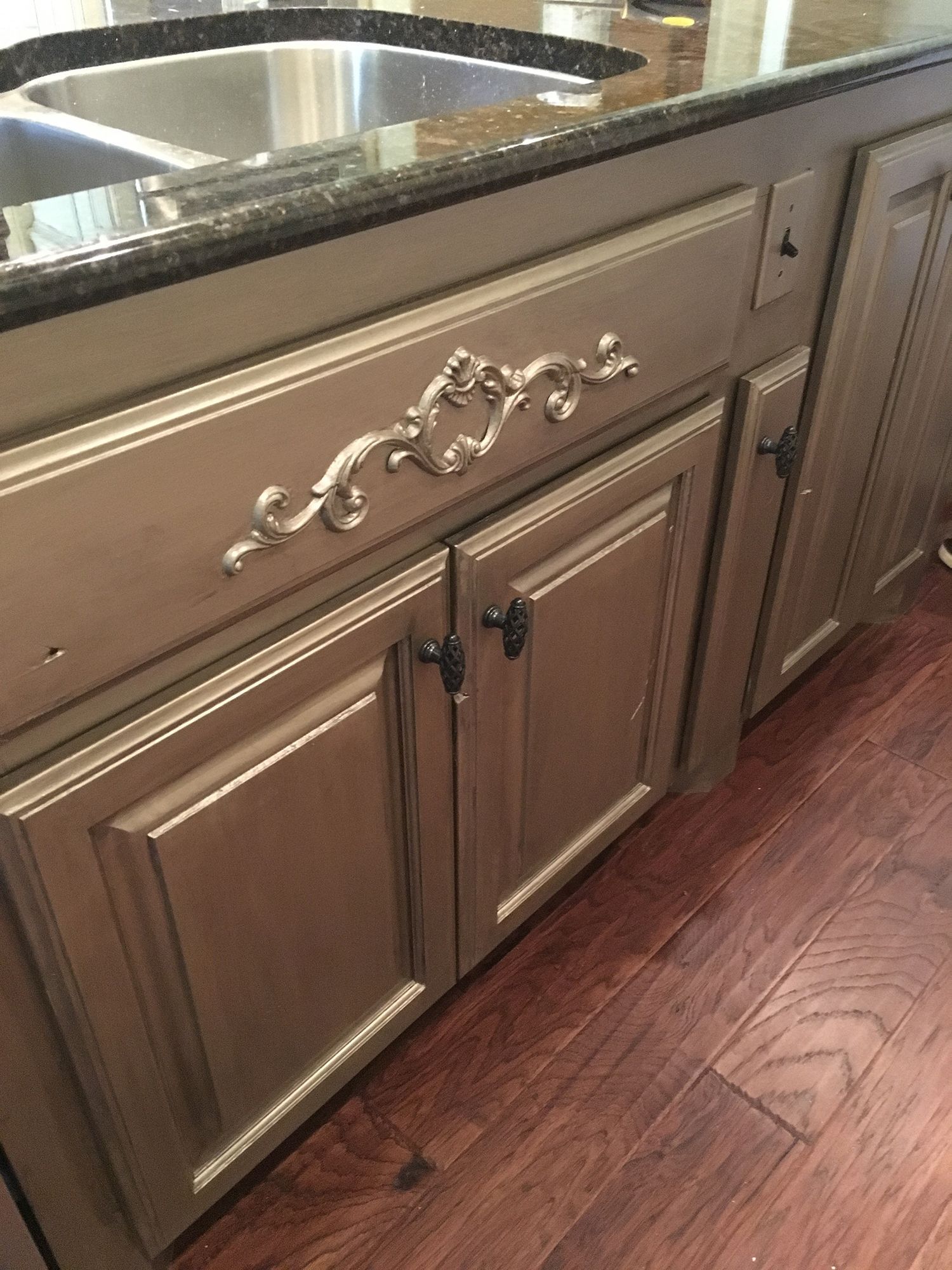Gold-painted kitchen cabinets with dark hardware and a decorative flourish on a dark countertop.