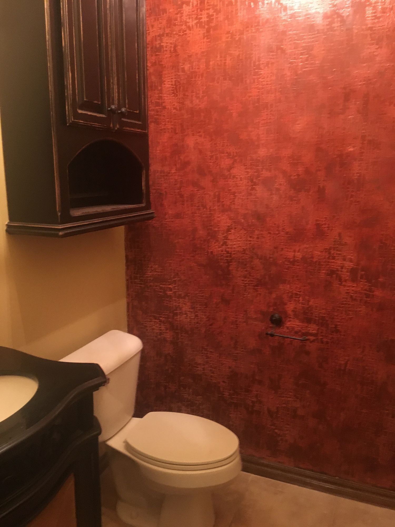 Bathroom with red textured wall, toilet, black cabinet, and vanity.