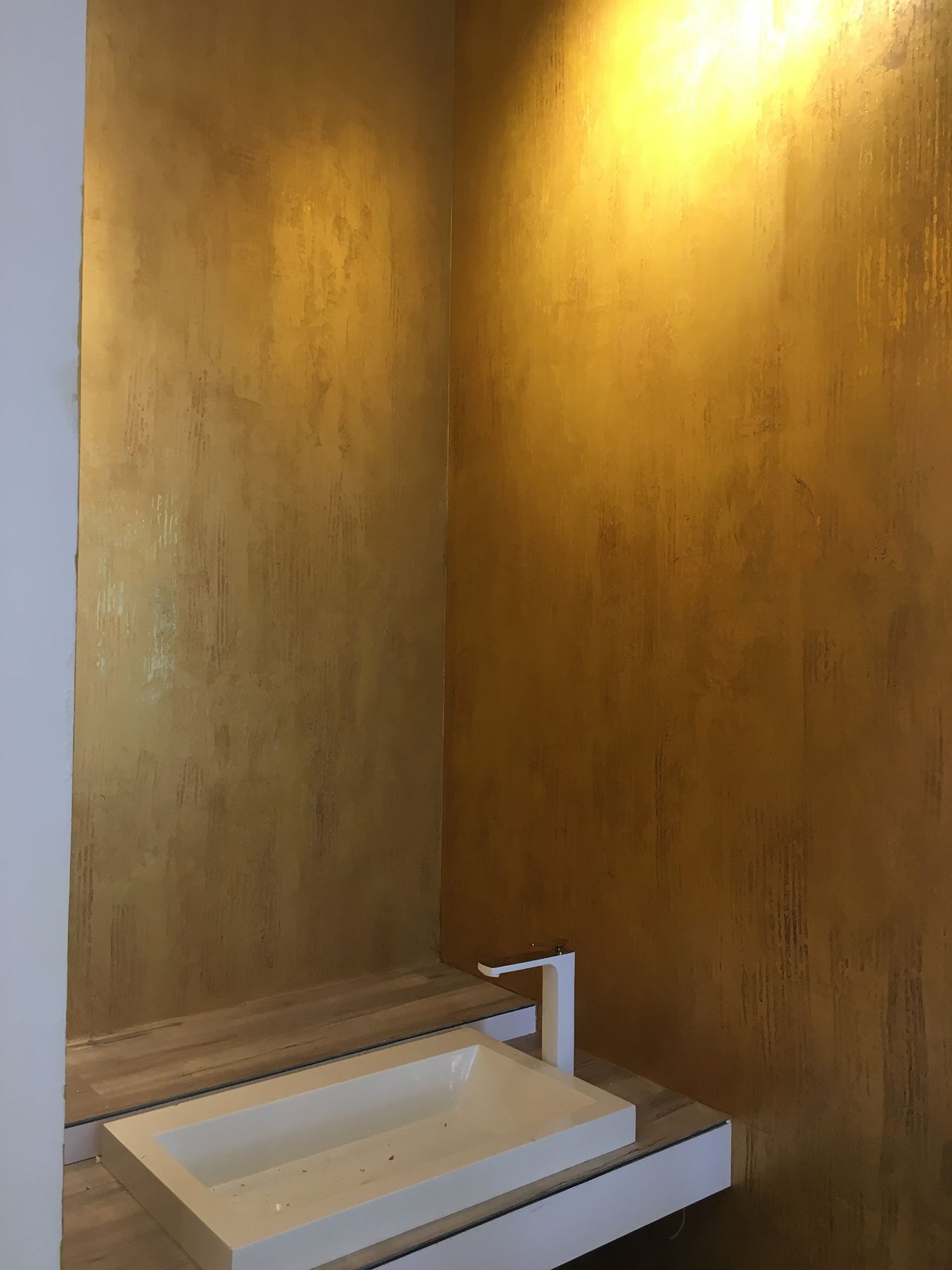 Gold-colored walls with a white sink and faucet, built into a wooden cabinet.