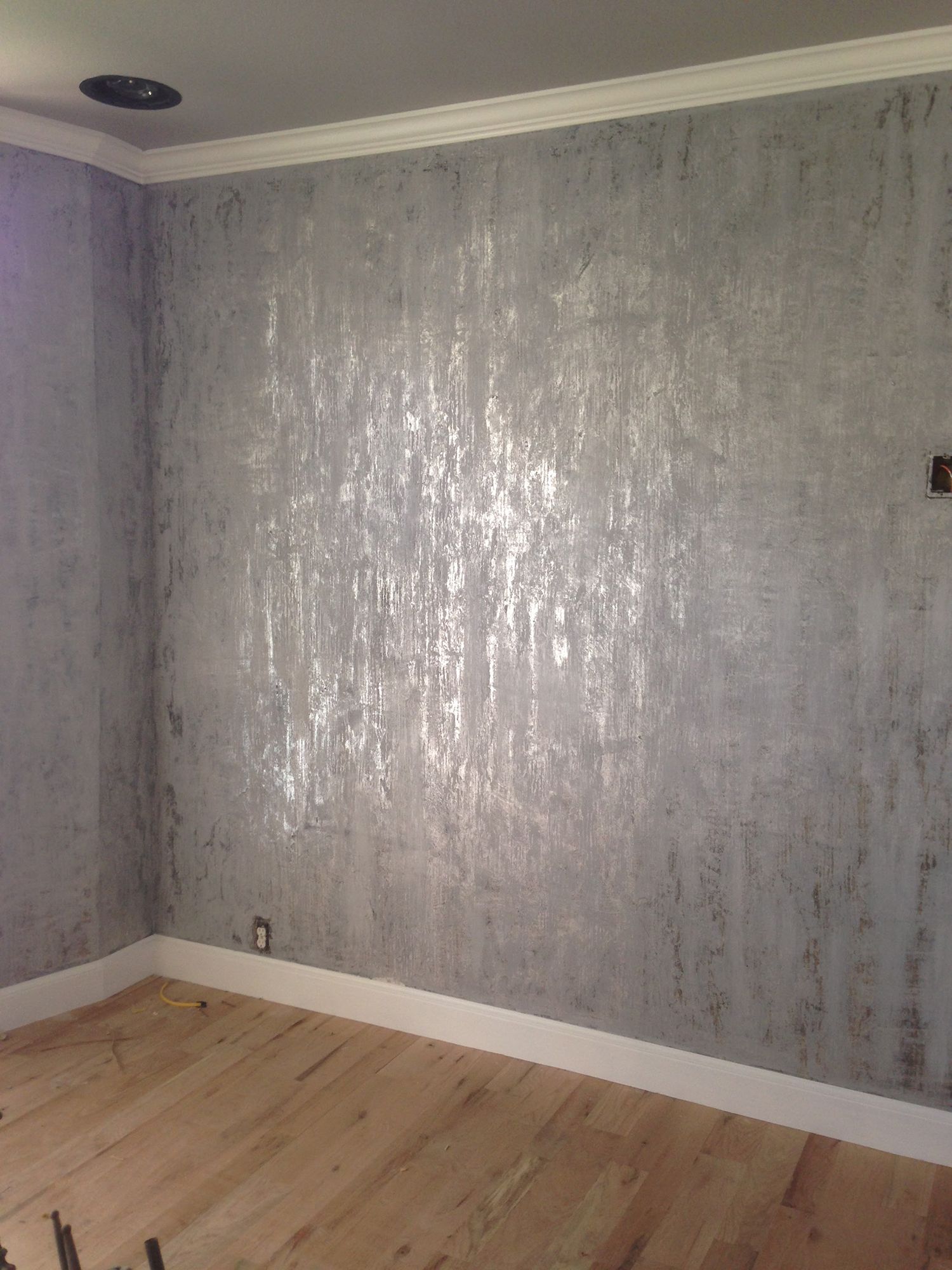Silver textured wallpaper on an interior wall with wood floor and white molding.