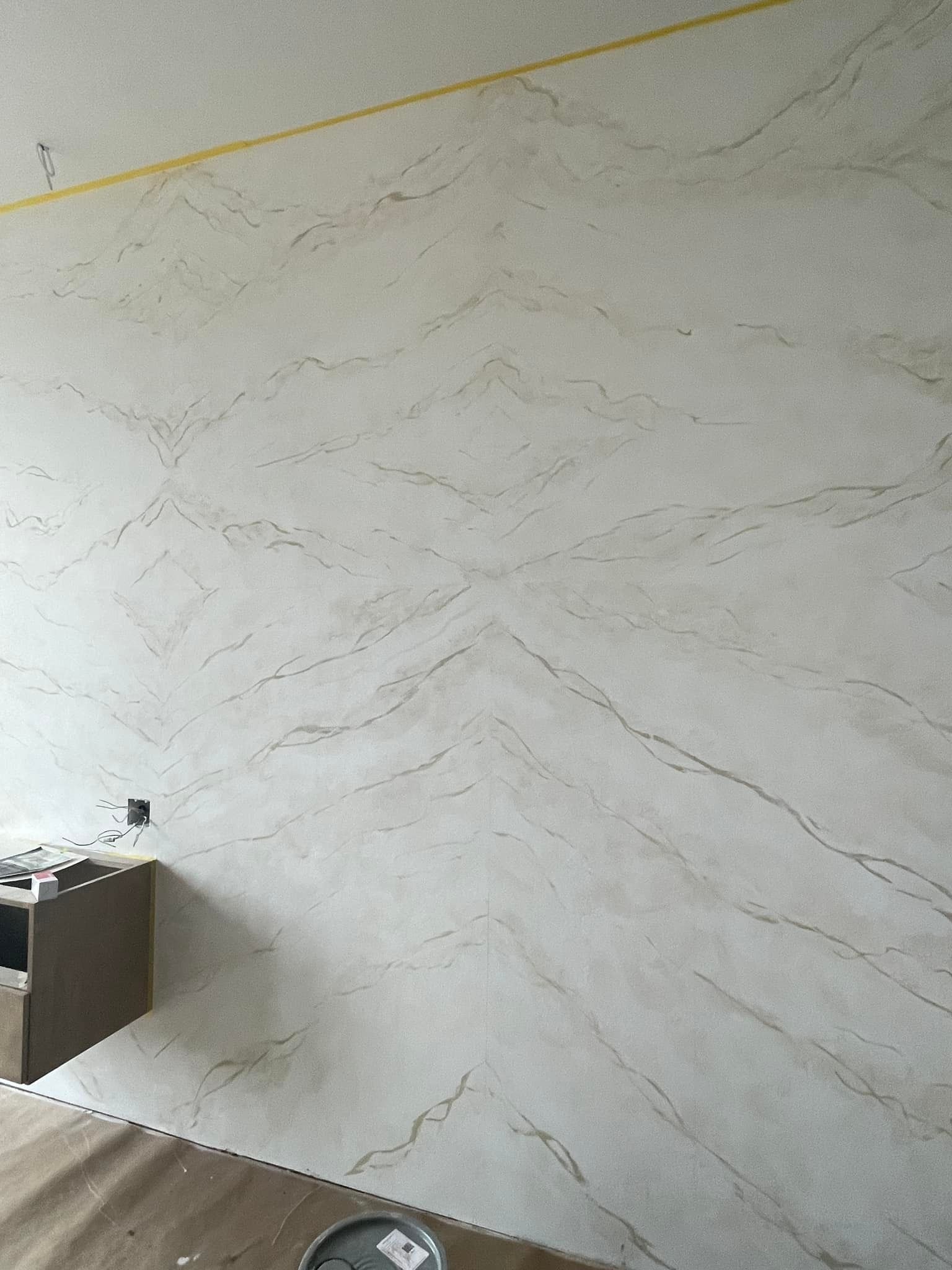 Off-white wall with veined marble effect. Wooden cabinetry at the base, and yellow tape along the top.