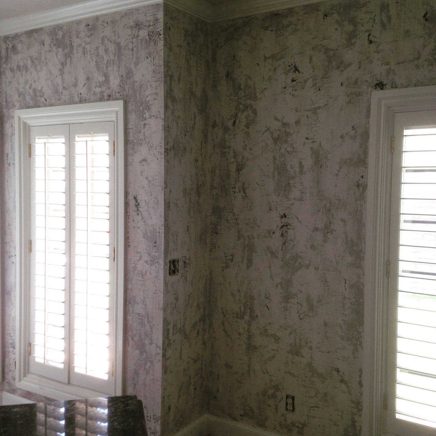 Room corner with textured, mottled gray and white walls; shuttered windows with white trim.