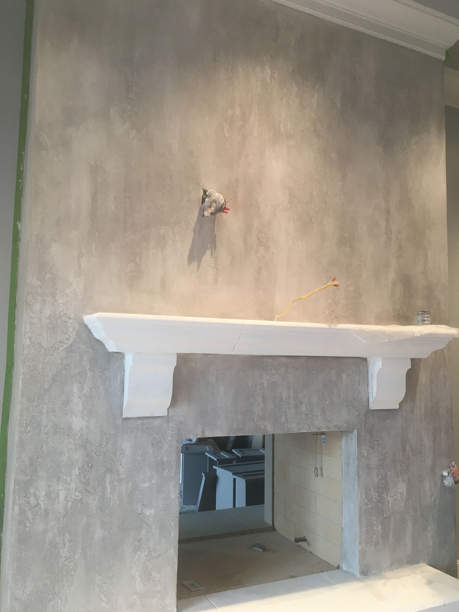 A gray, textured wall with a white mantle above a fireplace opening.