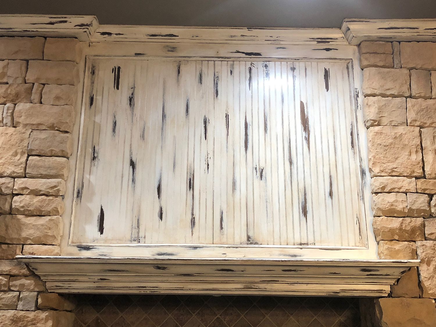 Whitewashed wooden panel on a stone wall, above a fireplace, with distressed paint effect.