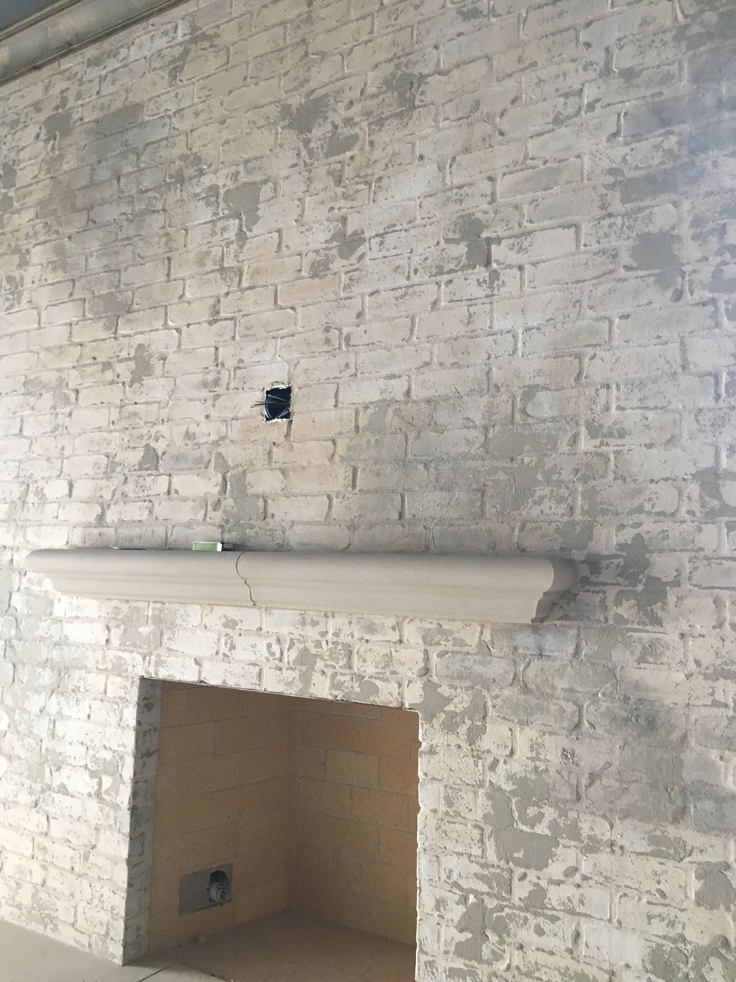 Brick fireplace with a partially plastered, painted white surface. A wooden mantel is installed.