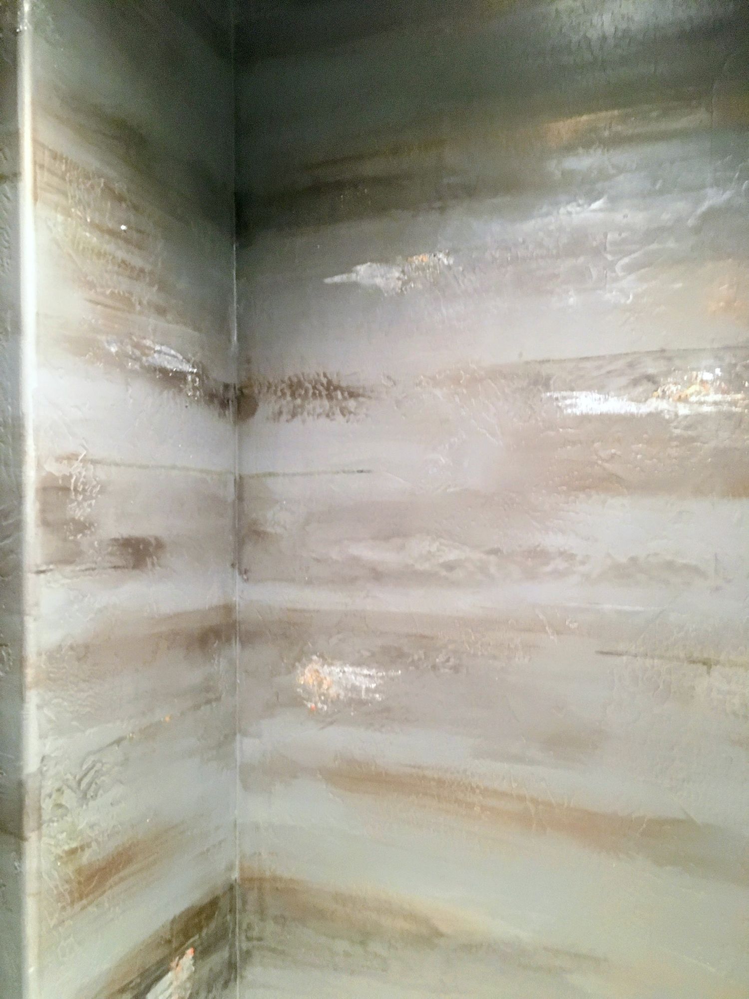 Corner of a wall with abstract, layered paint in brown, white, and gray tones.