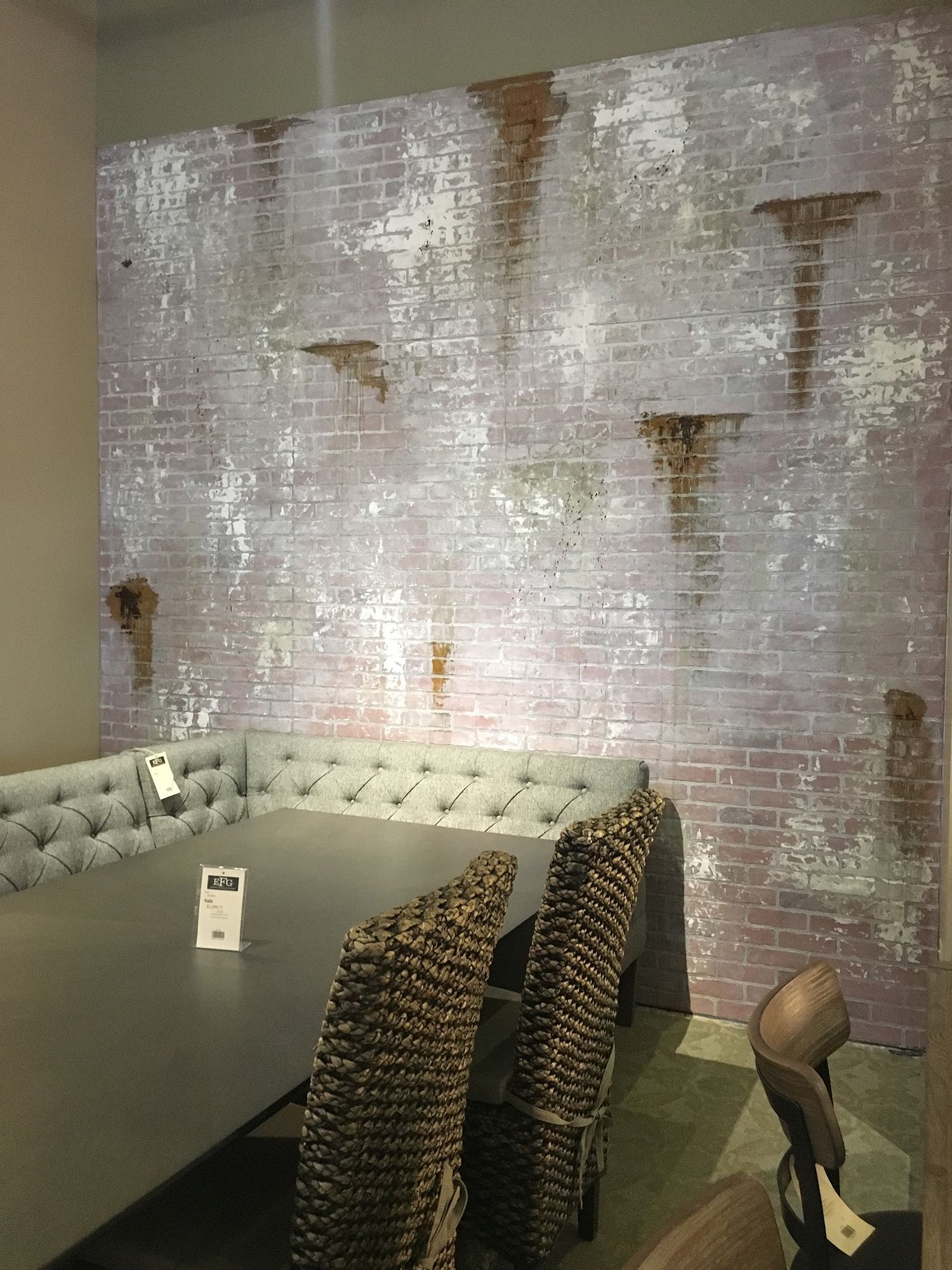 Dining room with gray table and chairs against a brick wall with water damage.