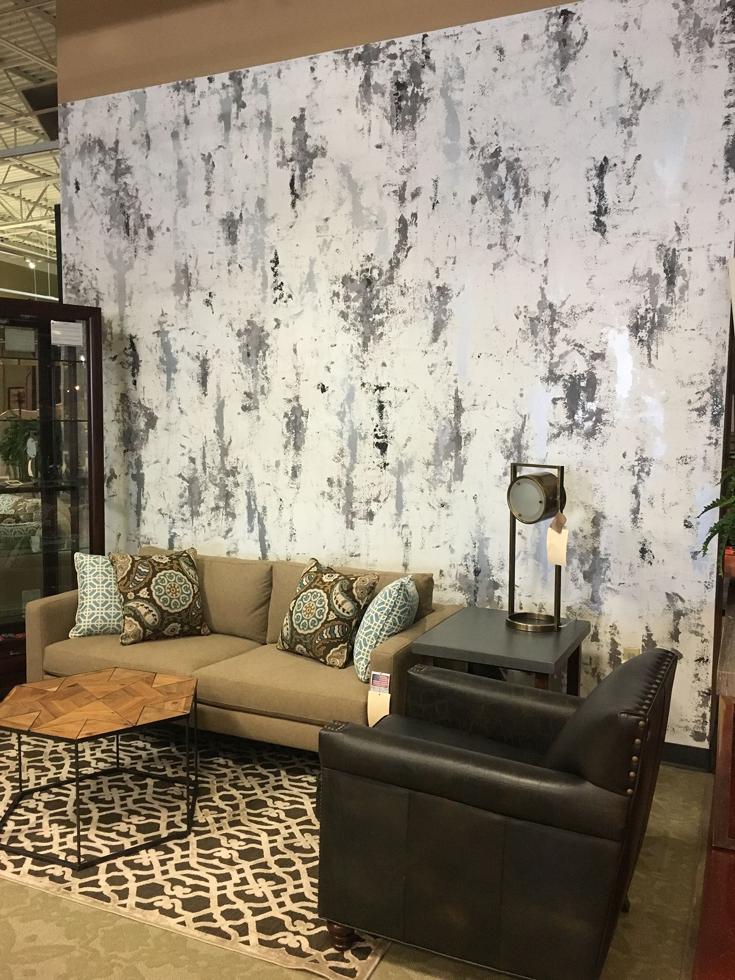 Living room setup: brown sofa, black leather chair, patterned rug, abstract wall art.
