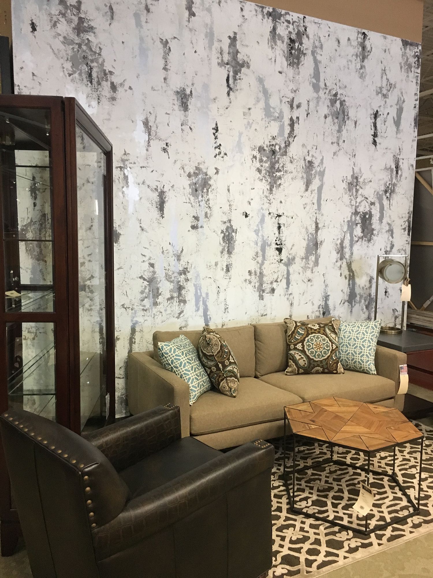 Living room with tan sofa, brown chair, glass cabinet, and abstract white, gray, and black wall art.