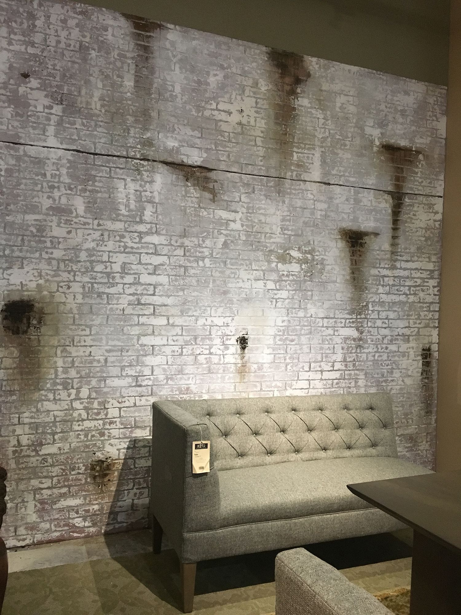 Gray tufted sofa against a distressed white brick wall with rust stains.