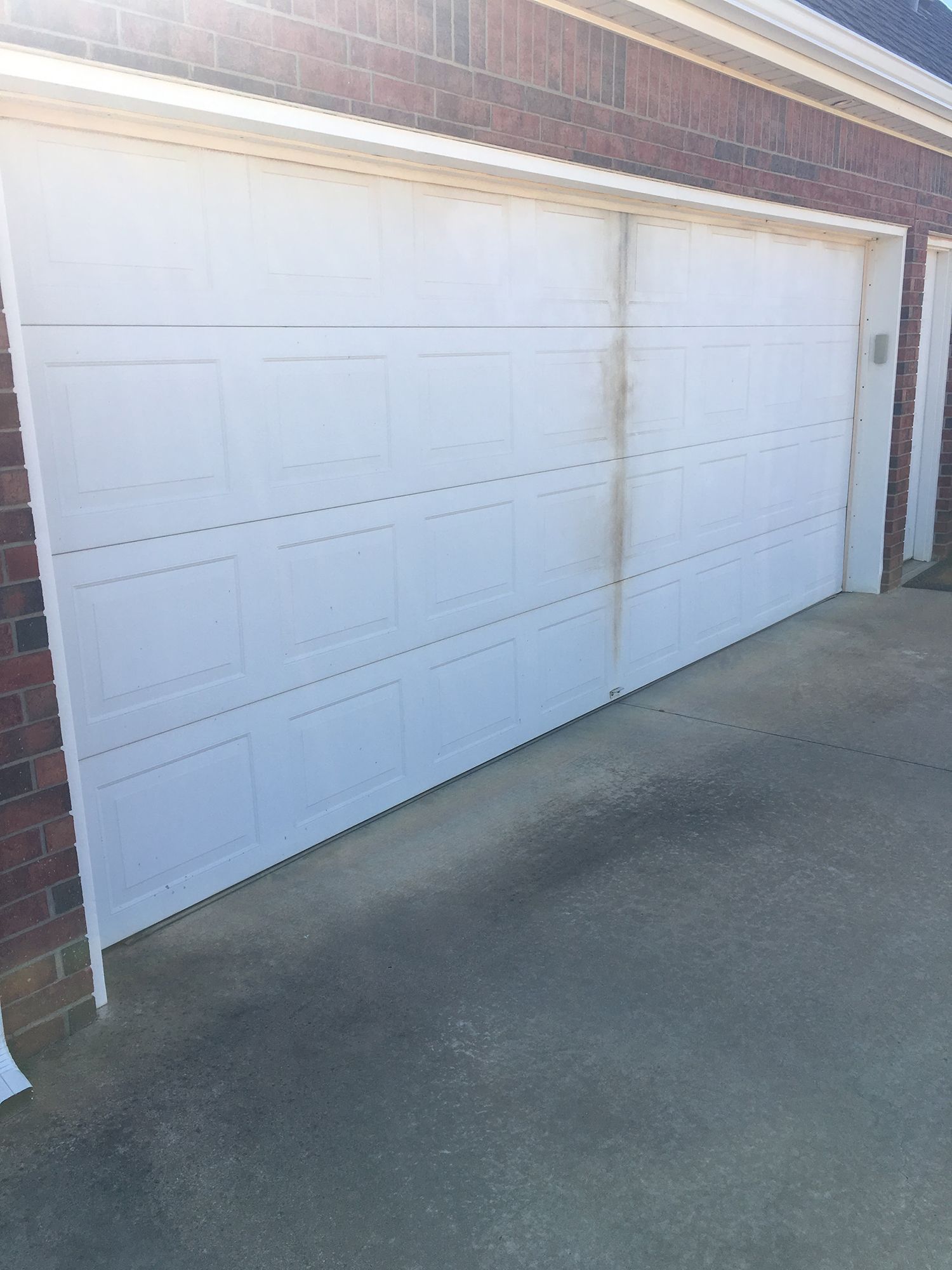 White garage door with dirt and discoloration, in front of a brick building.