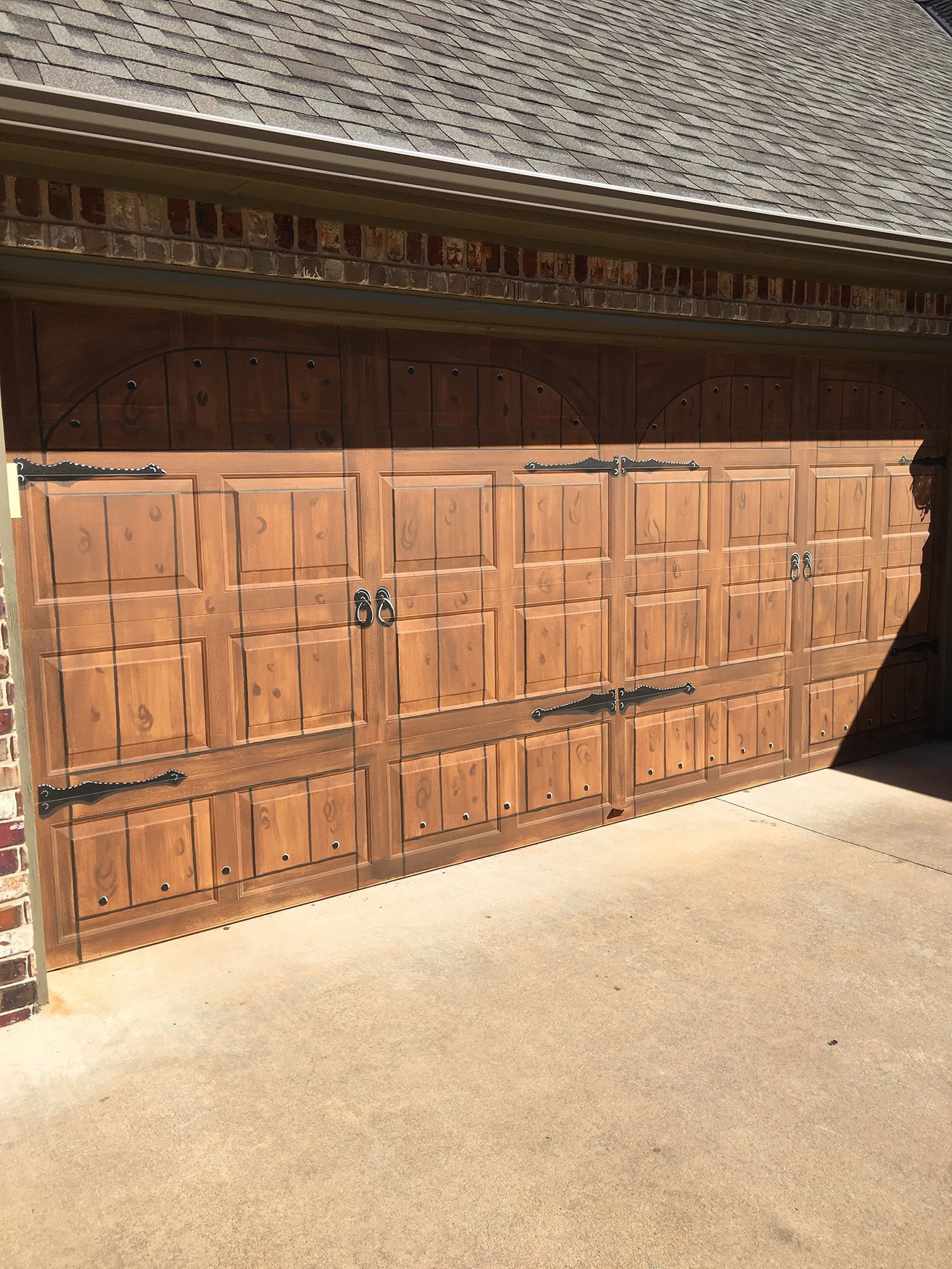 Wooden garage door with decorative hardware. Brickwork and brown shingles above.