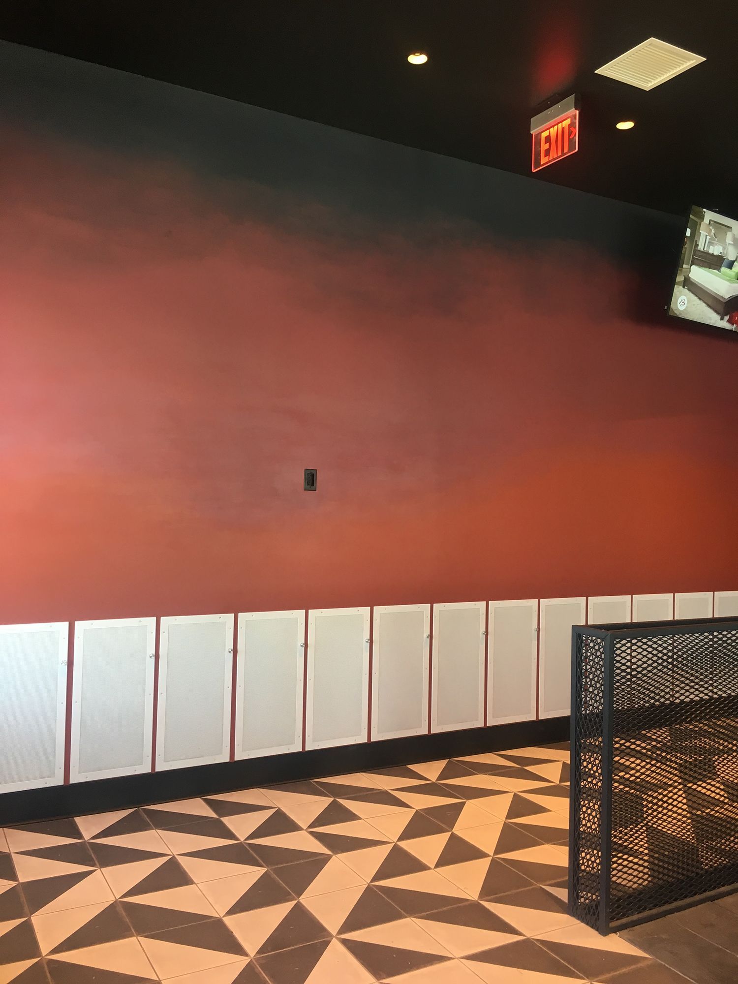 Interior of a bar with a patterned floor, red and black wall, and white paneling. An exit sign is visible.