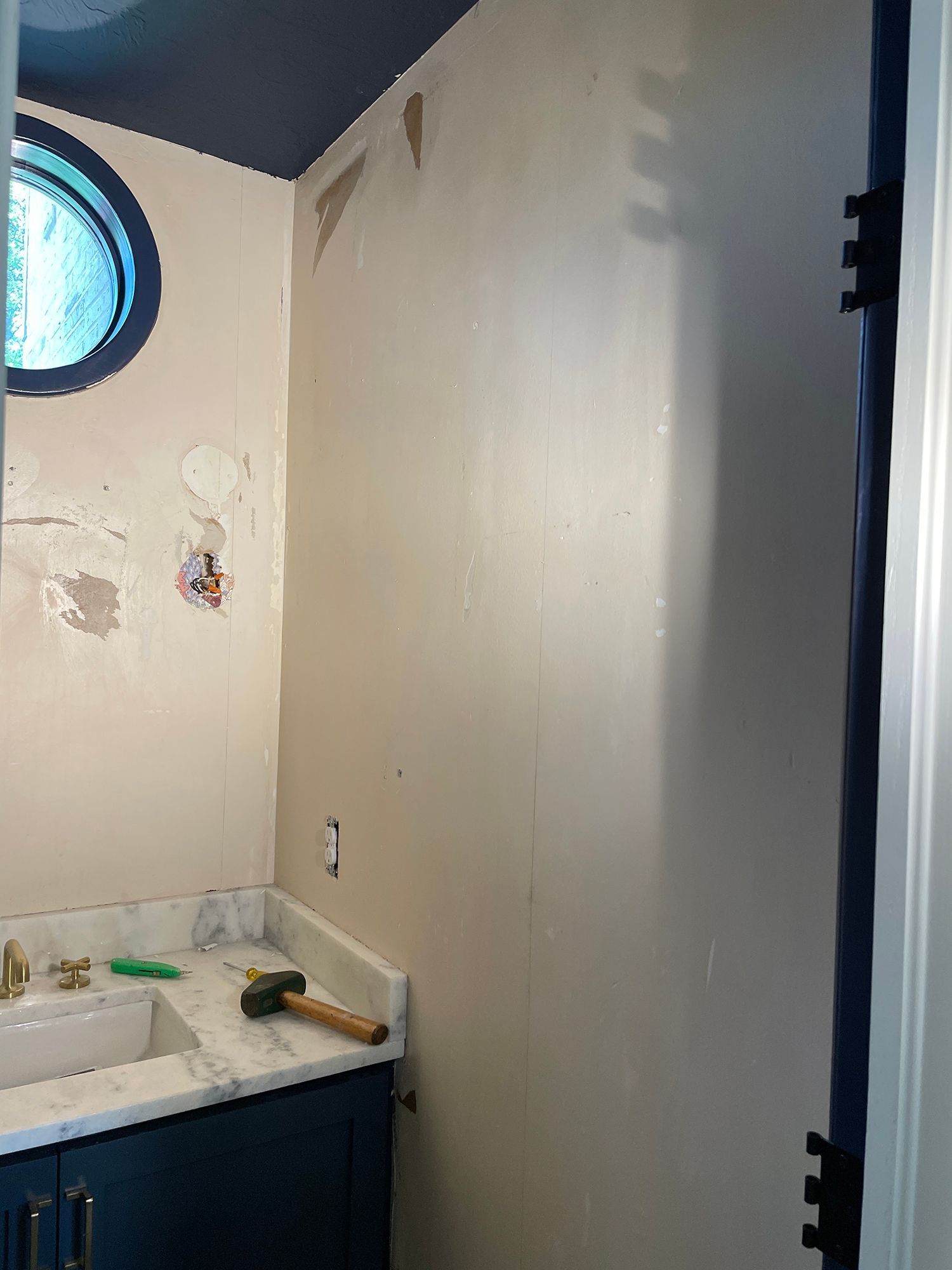 Bathroom interior with a vanity, round window, and wall repair work.