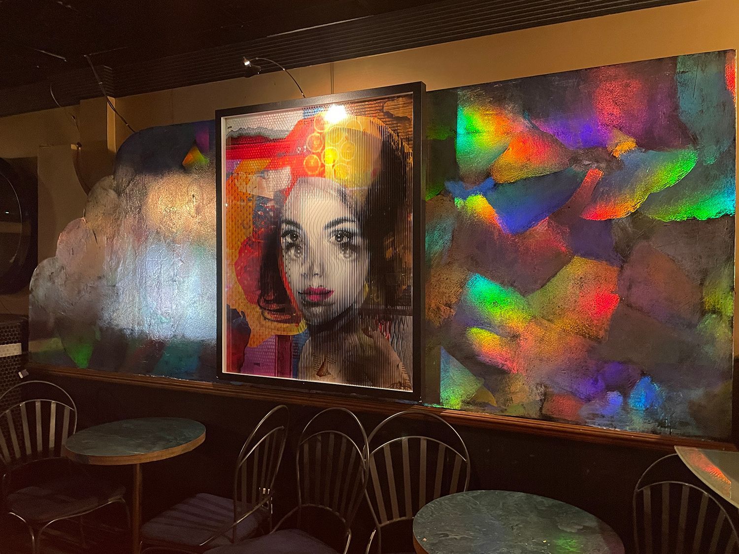 Bar interior with art and tables. Abstract painting of woman's face between reflective panels. 