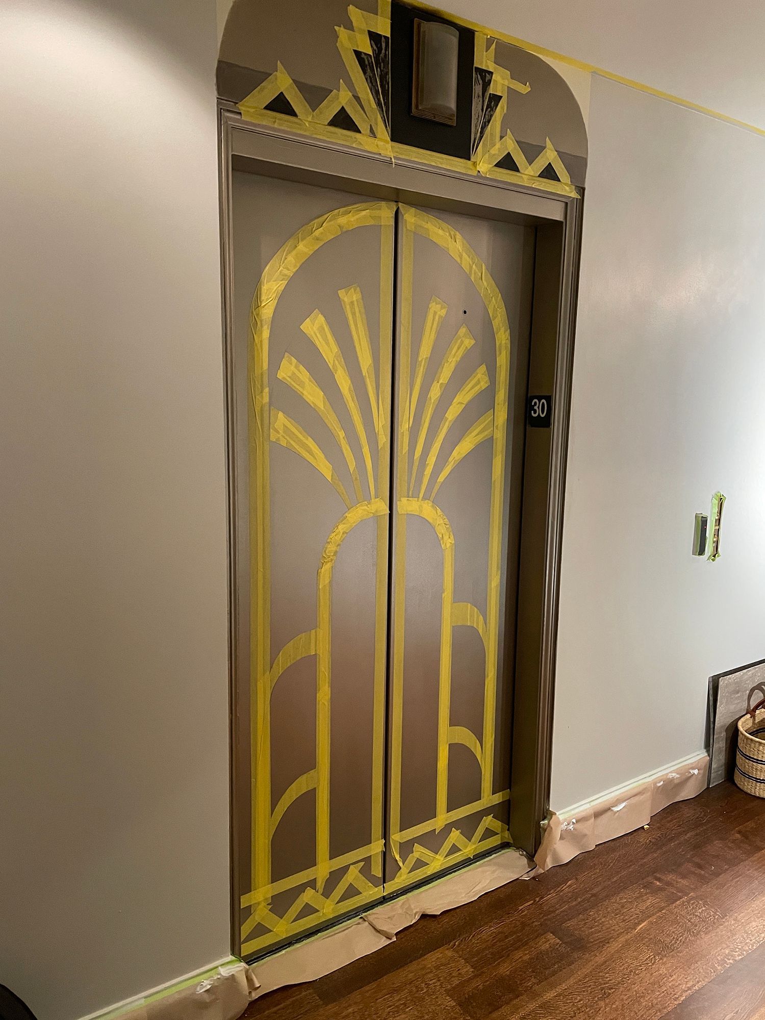 Elevator doors painted with a gold art deco design in a hallway.