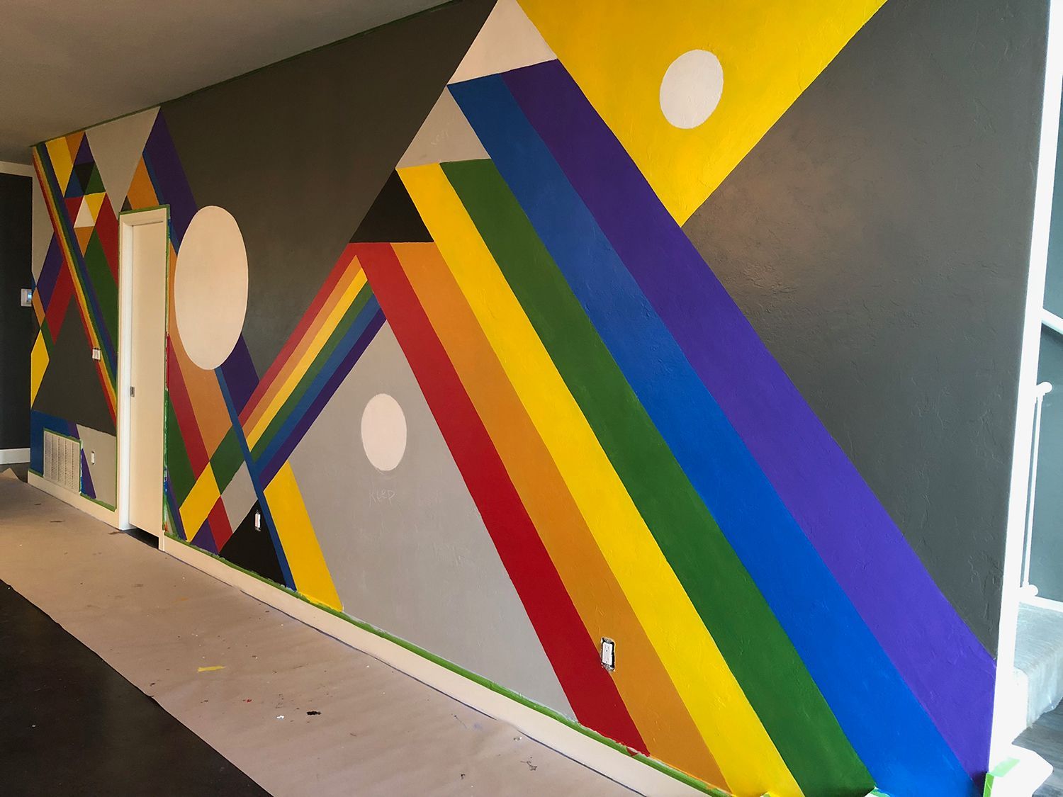 Colorful geometric mural on a gray wall, featuring prisms and circles.