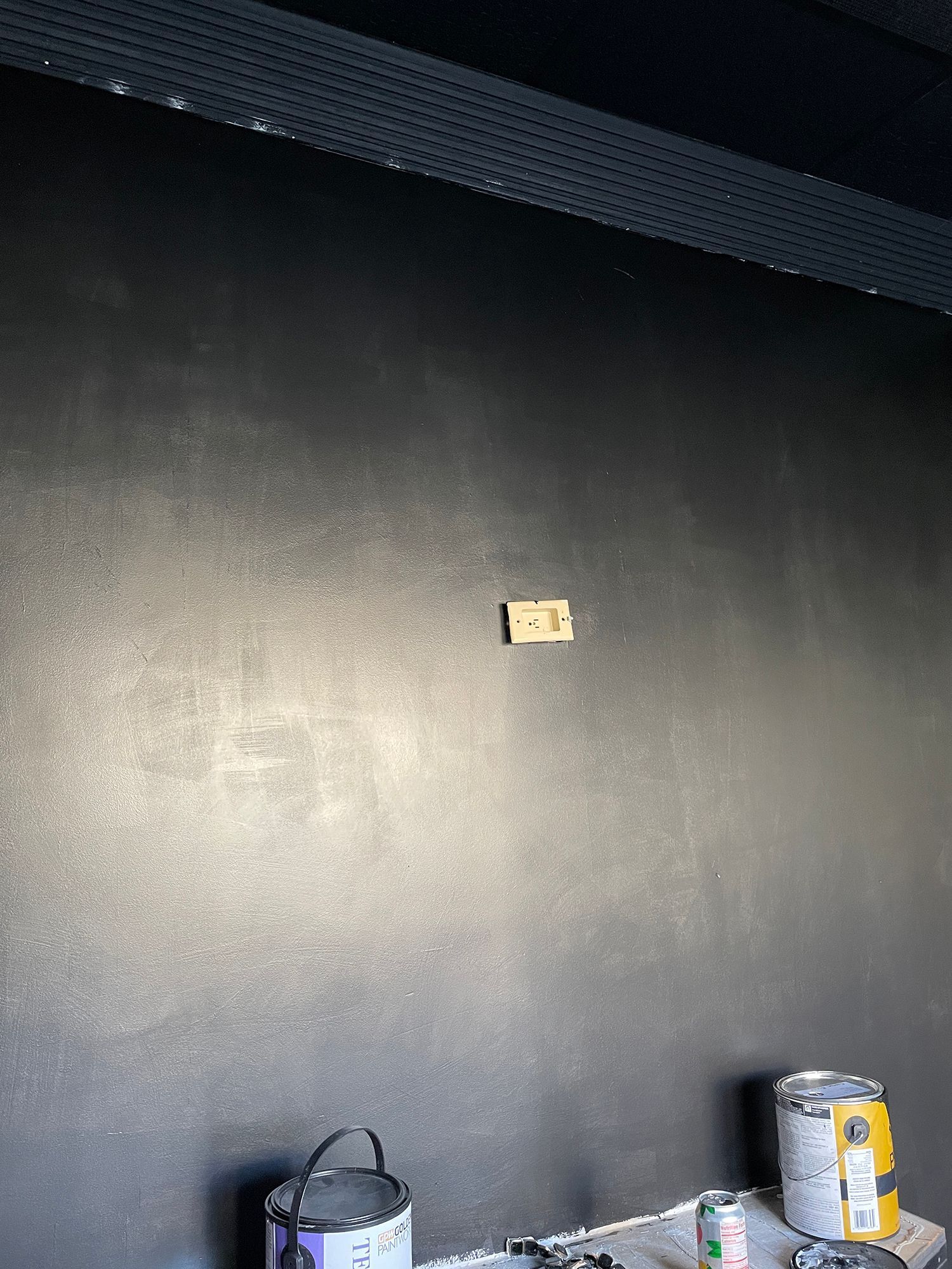 Black painted wall with wooden block, paint cans, and dark ceiling trim.