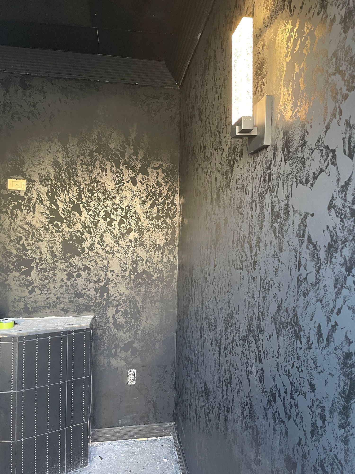 Dark textured walls in a room, with a modern wall light.