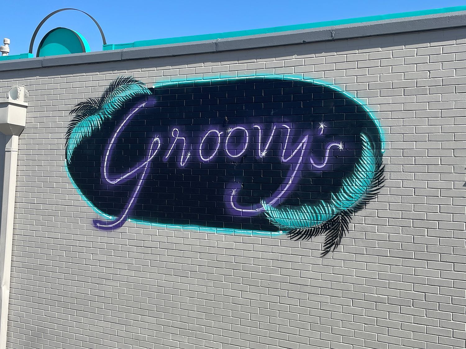 Groovy's neon sign on a gray brick wall.