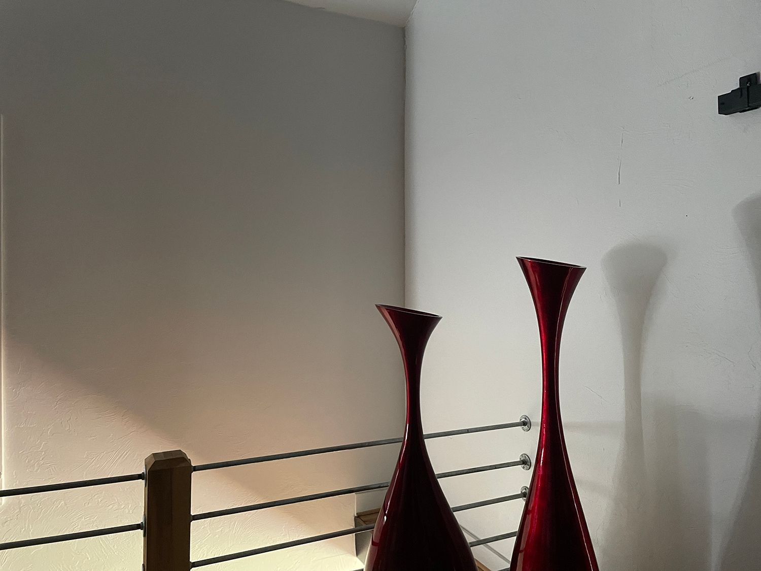 Two red vases on a railing, against a white wall.