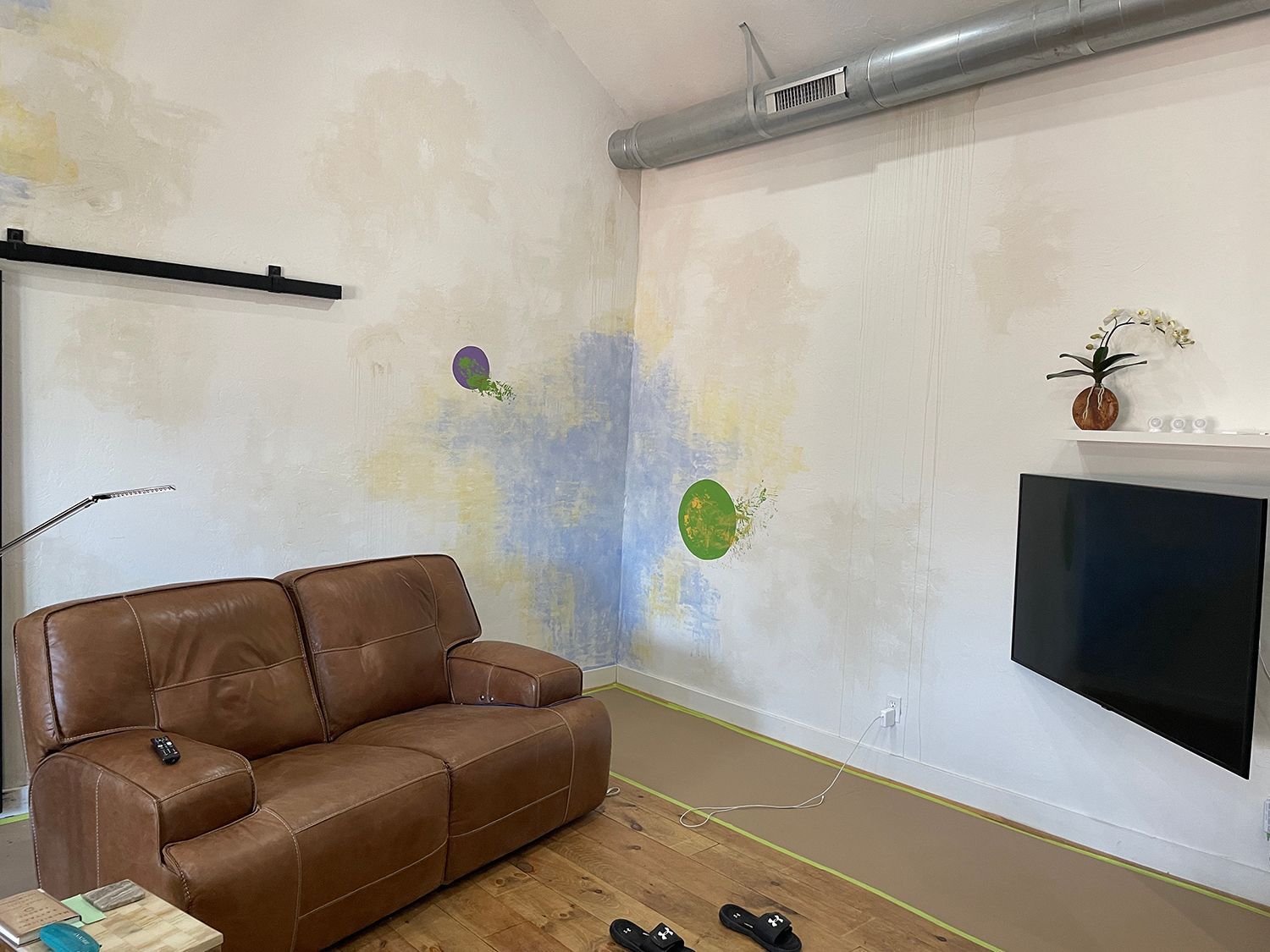 Living room with brown leather sofa, TV, and wall with abstract paint designs.