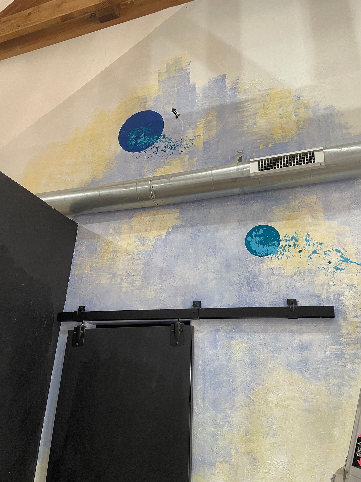 Wall with painted blue circles and splatter-like accents, above a black sliding door and metal pipe.