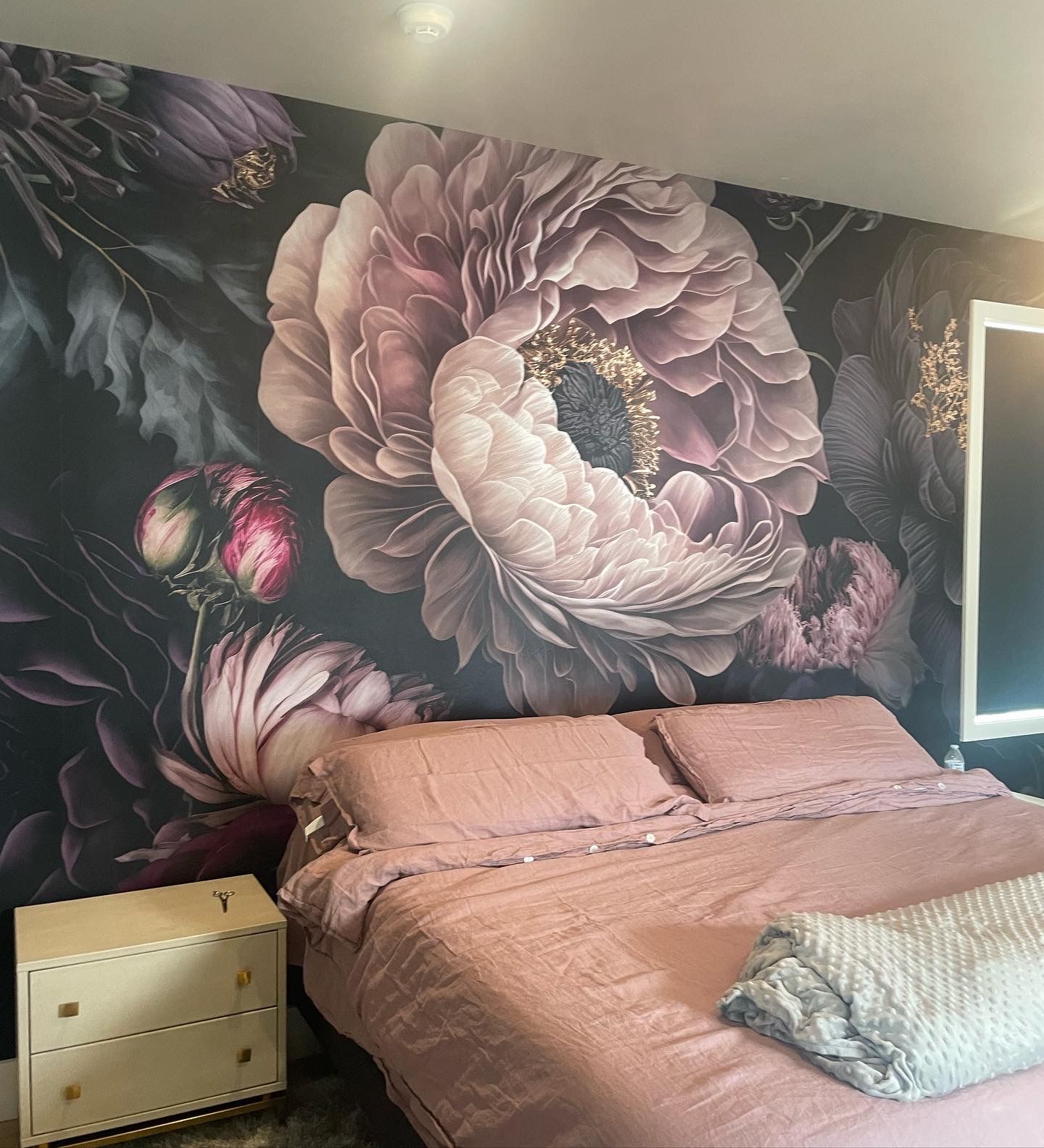 Bedroom with floral wallpaper and pink bedding. A bedside table sits to the left of the bed.