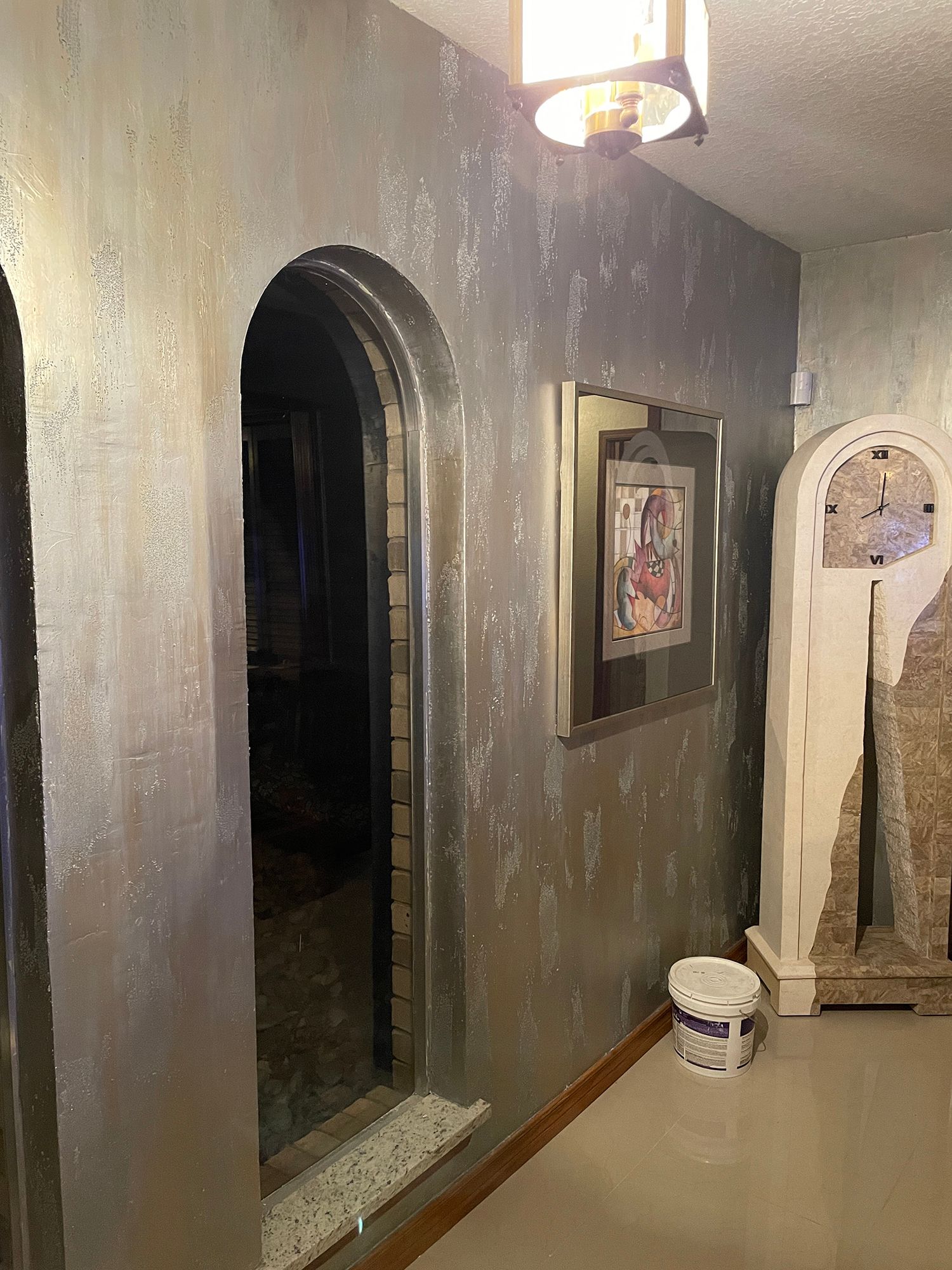 Hallway with textured silver walls, arched doorway, framed artwork, and grandfather clock.