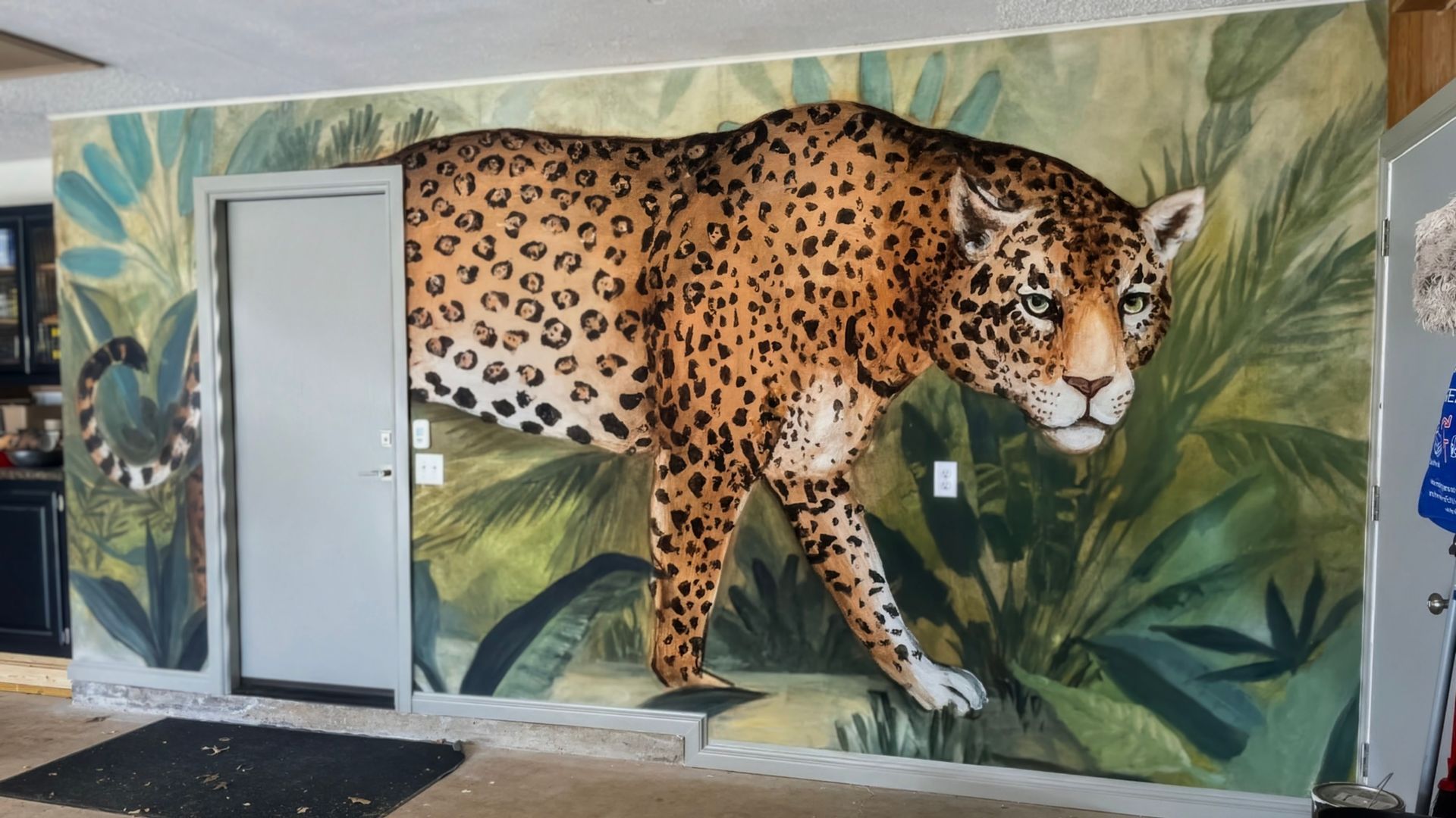 Mural of a jaguar emerging from jungle foliage on a wall with a door.