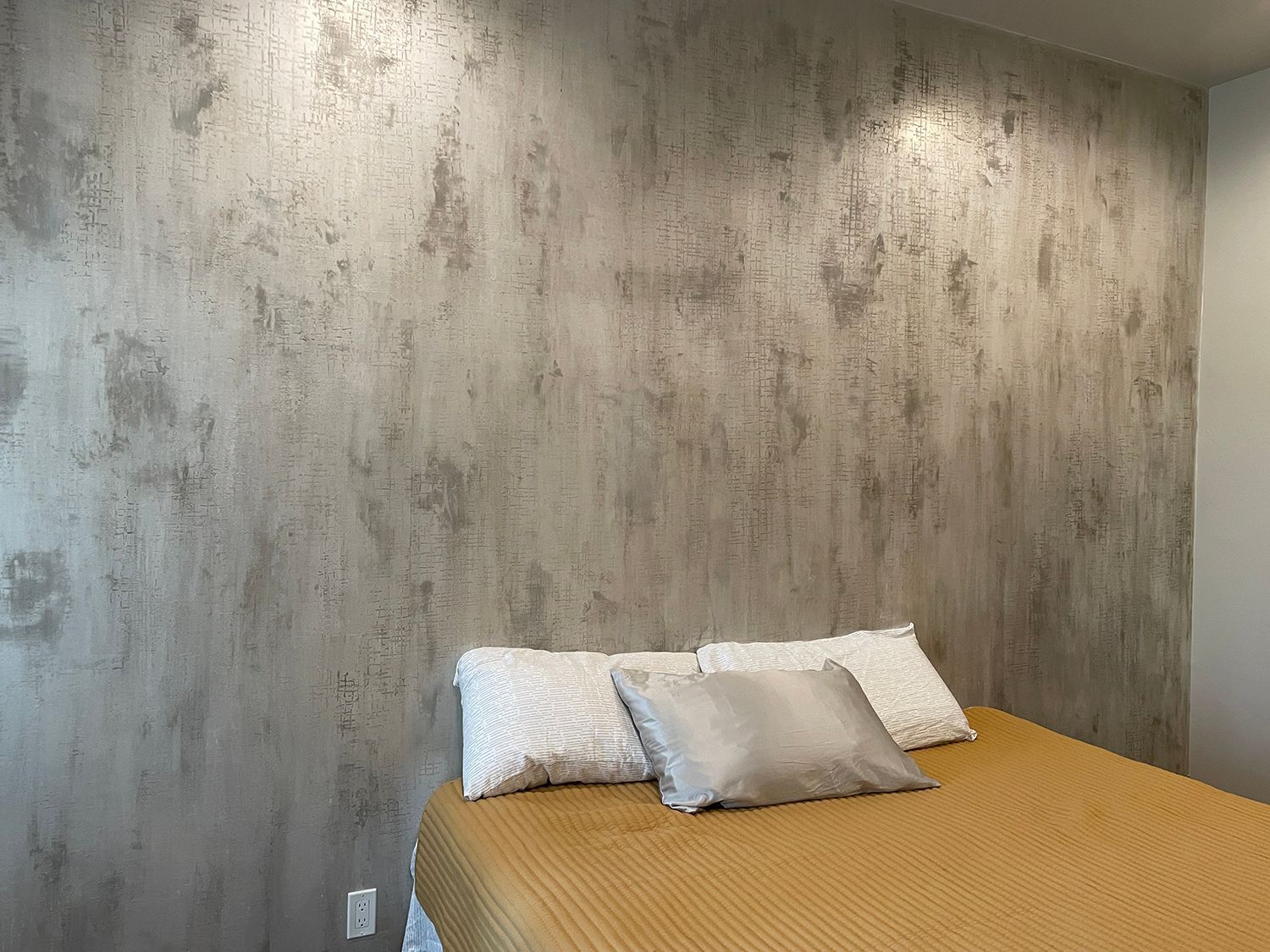 Bedroom with bed, pillows, and textured gray accent wall.