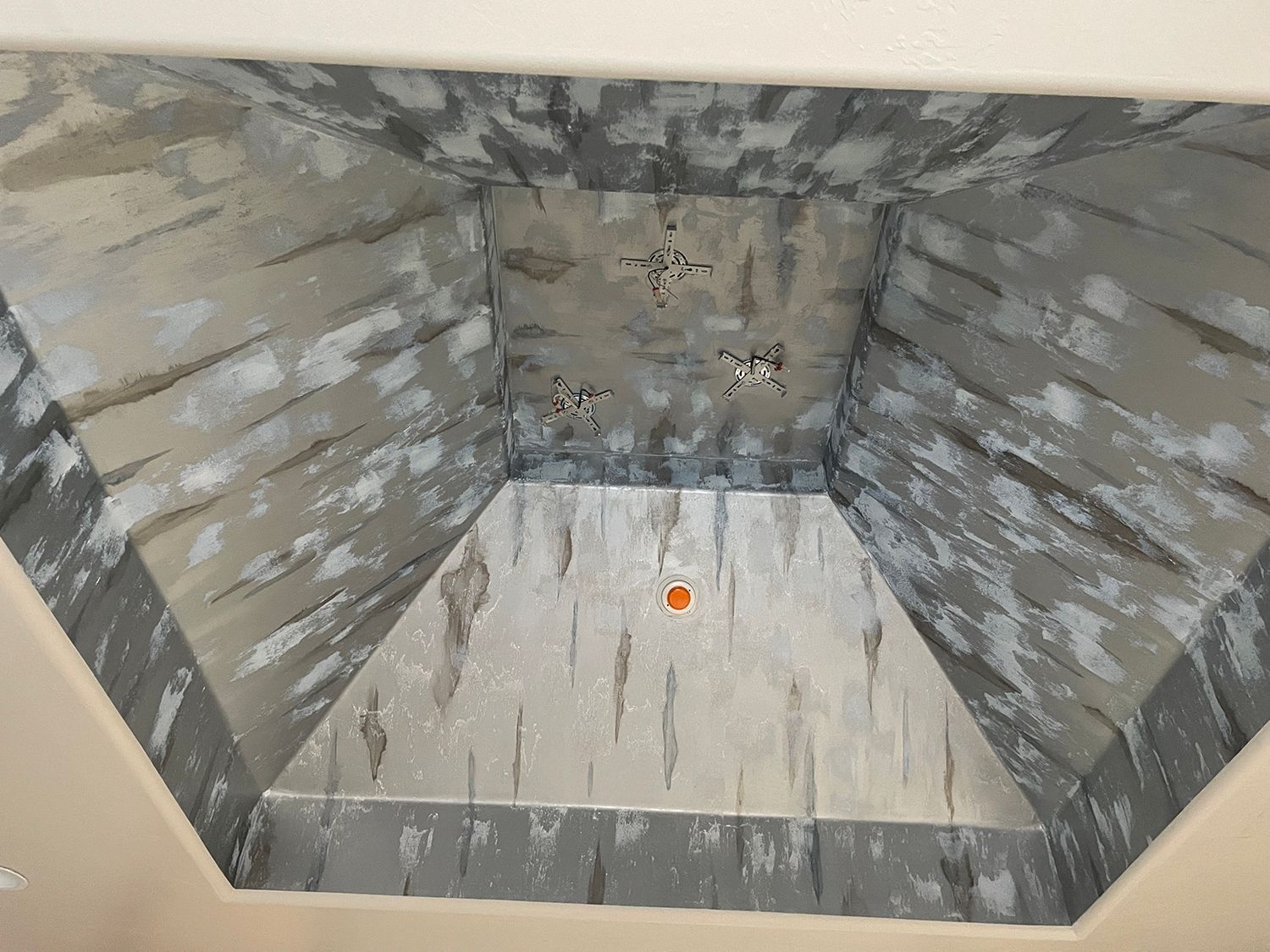 Gray and white textured ceiling with inset pyramid shape and orange light.