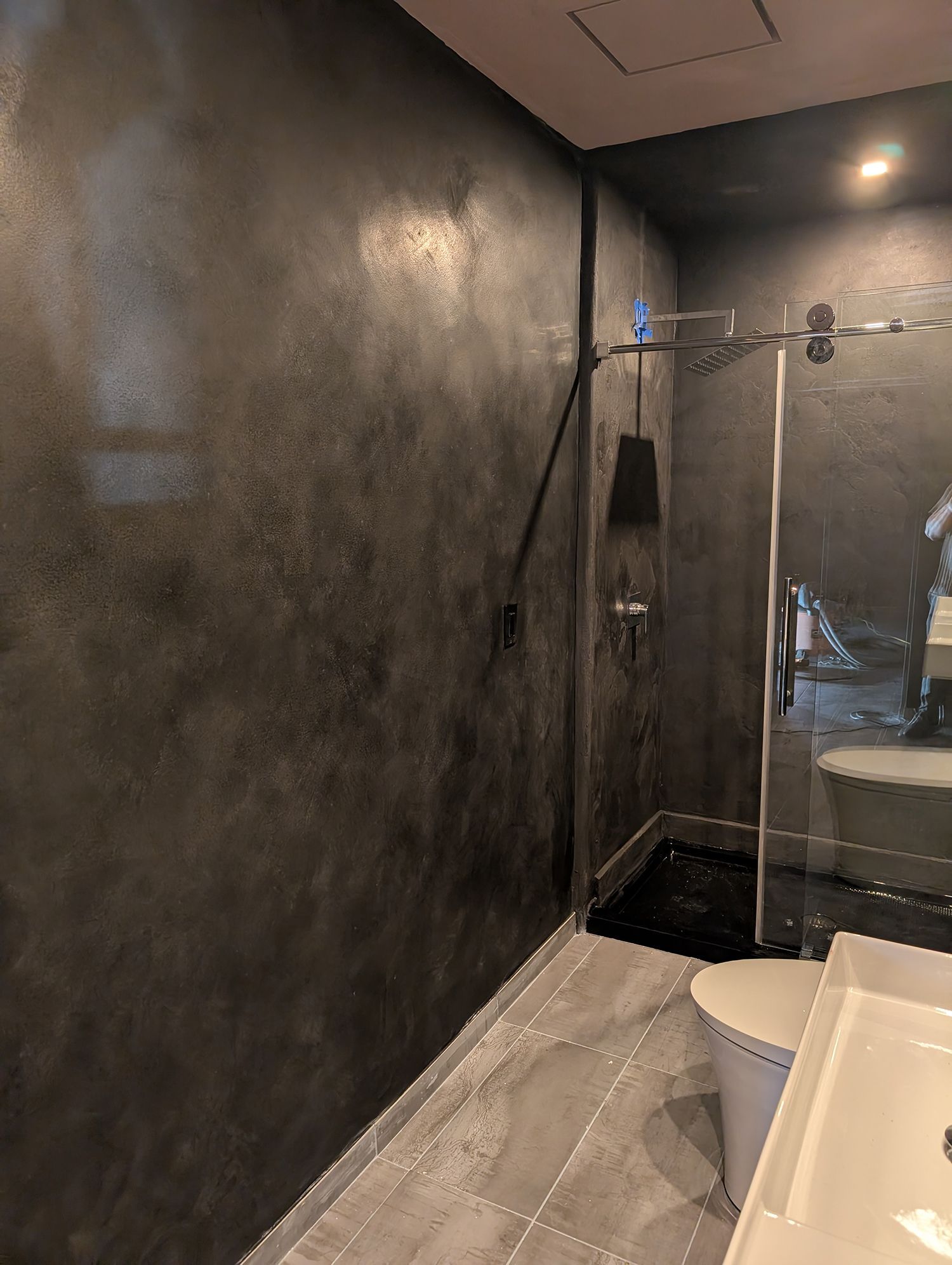 Dark gray bathroom with textured walls, glass shower, and white toilet.