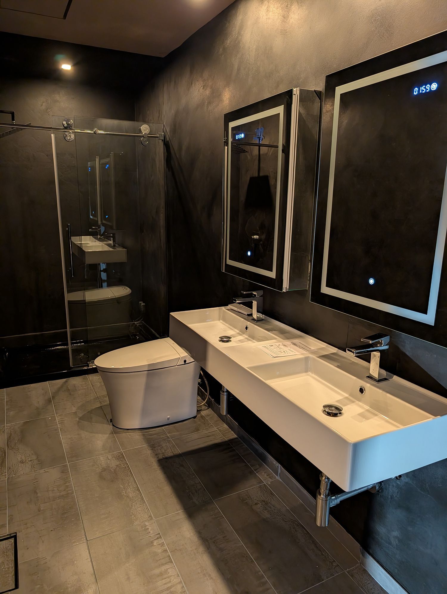 Modern bathroom with floating double sink, lit mirrors, glass shower, and toilet.